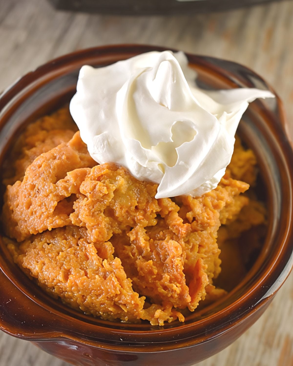 Creamy slow cooker pumpkin pie pudding topped with a generous dollop of whipped cream in a brown bowl, perfect for crockpot thanksgiving recipes.