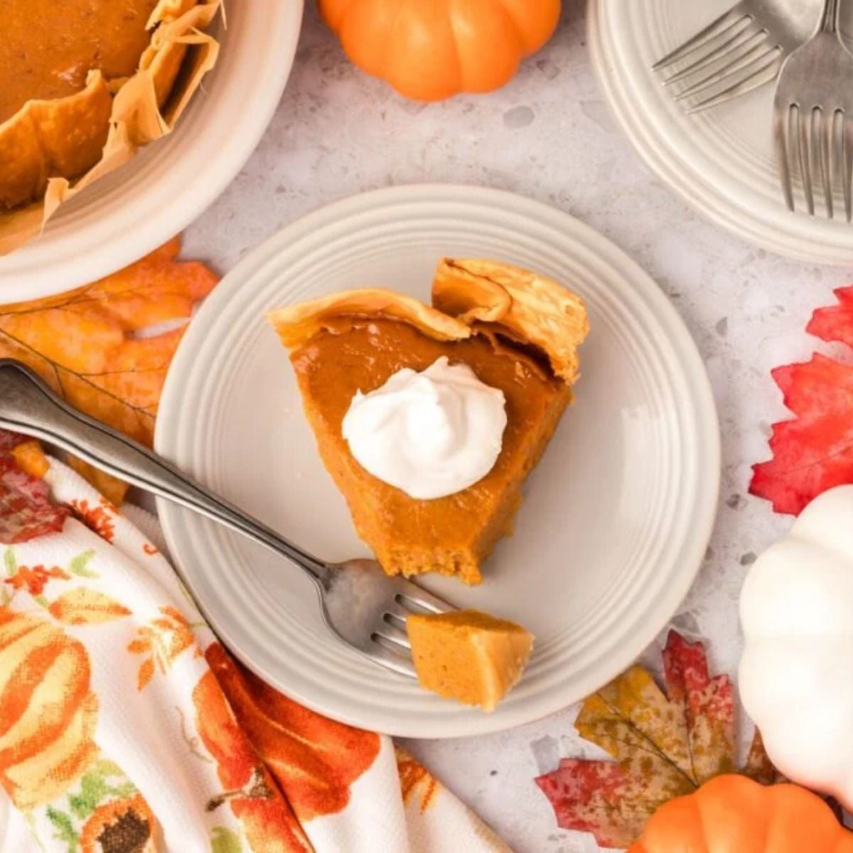 Slice of smooth crockpot pumpkin pie topped with whipped cream served on a plate surrounded by autumn leaves, perfect for crockpot thanksgiving recipes.