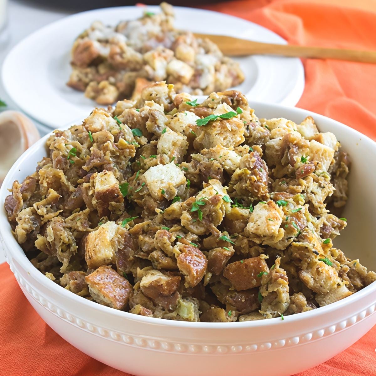 Savory crockpot stuffing thanksgiving recipe with herbs served in a large white bowl over an orange napkin.