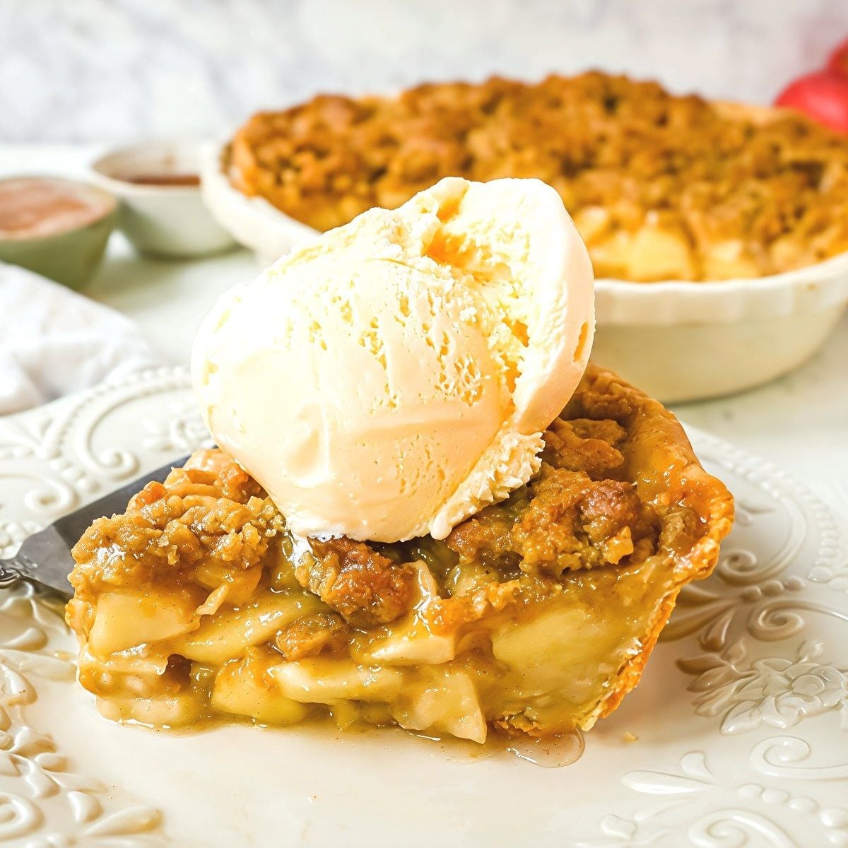 A warm slice of Dutch apple pie layered with tender cinnamon apples and a golden brown streusel topping, served ala mode with a scoop of vanilla ice cream.