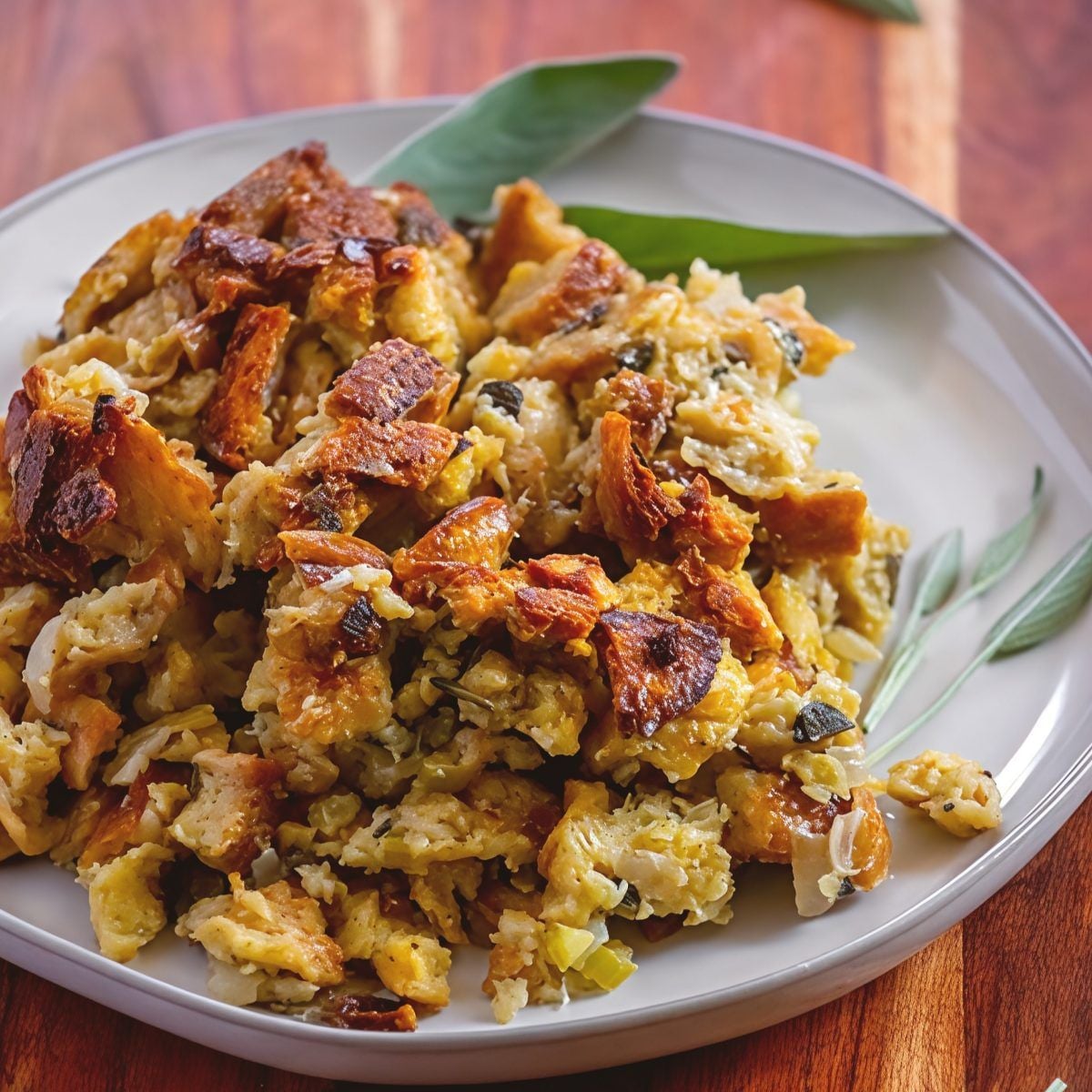 A serving of easy crockpot stuffing thanksgiving recipe garnished with fresh sage leaves on a grey ceramic plate over a wooden table.