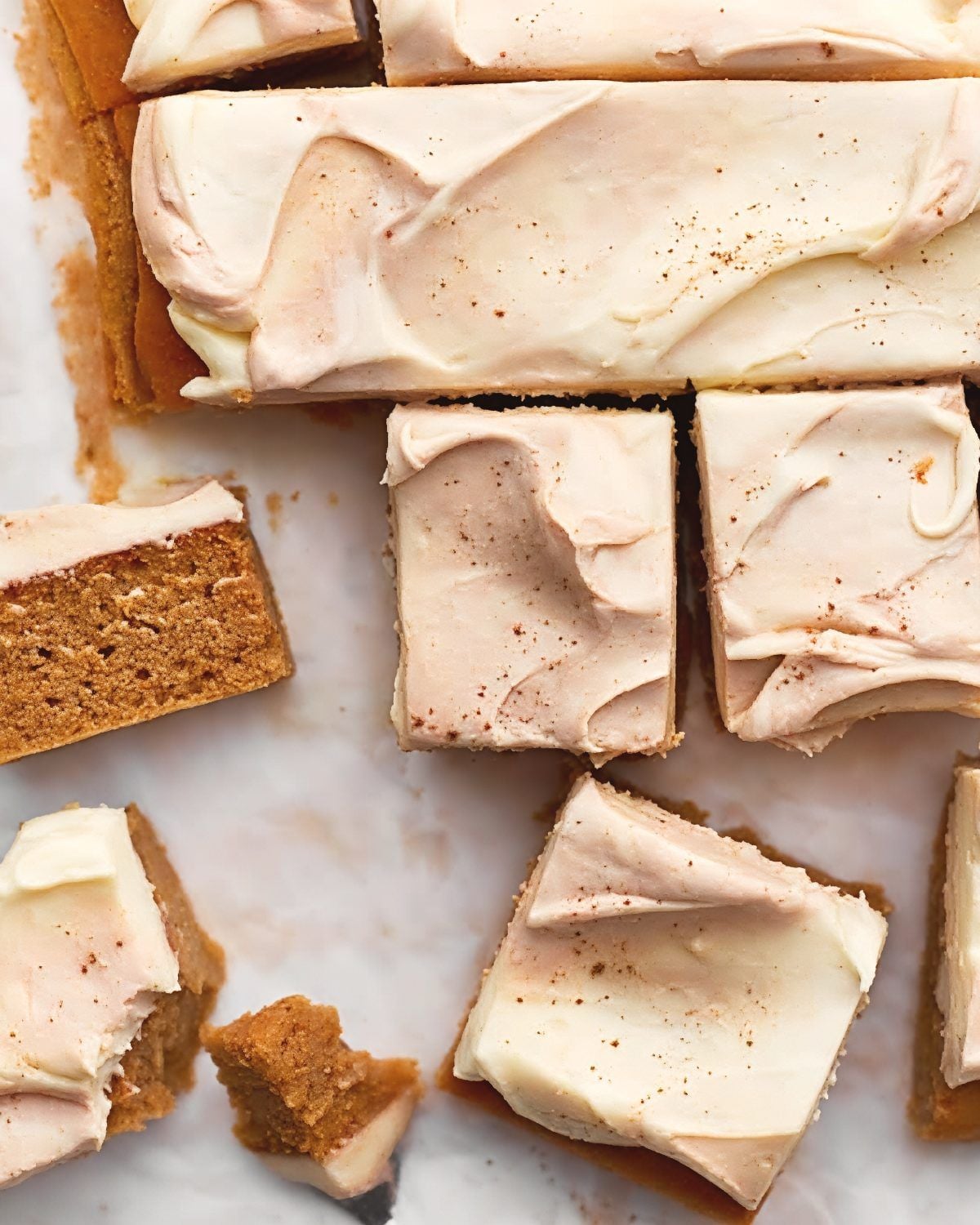 Moist, square-cut slices of homemade pumpkin spice cake topped with thick, swirled cream cheese frosting and a light dusting of cinnamon.