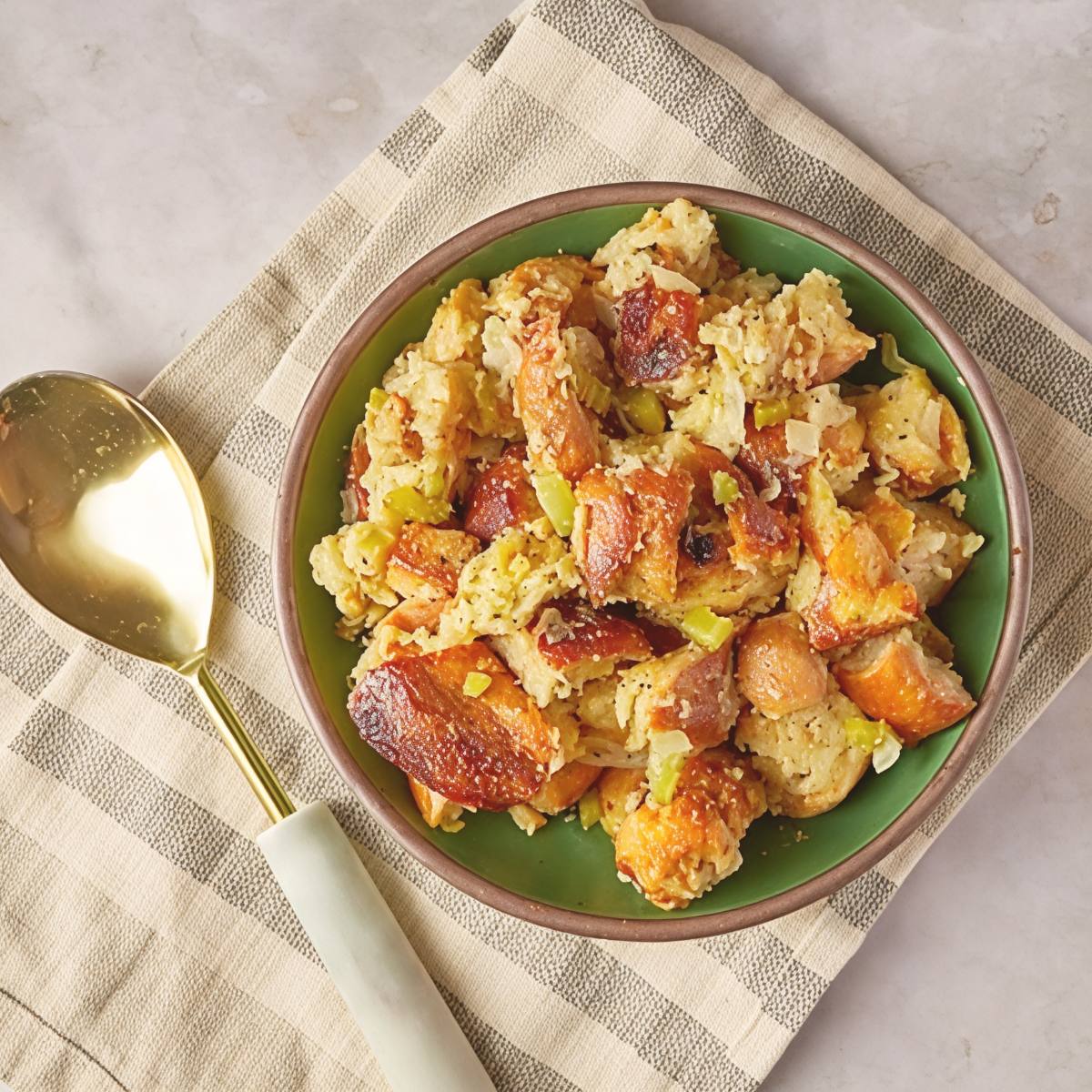 Easy crockpot stuffing thanksgiving recipe served in a green bowl with a gold spoon on a striped napkin.