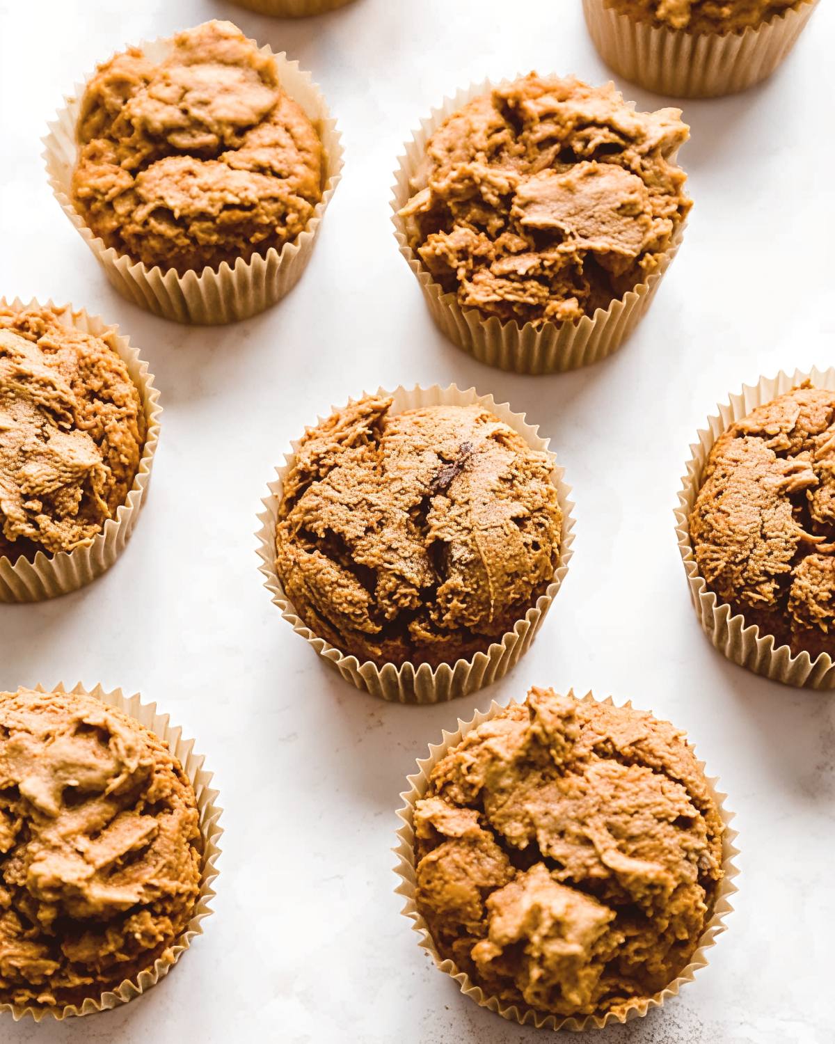 Freshly baked 2-ingredient pumpkin muffins in paper muffin liners arranged on a white surface for an easy Thanksgiving dessert.