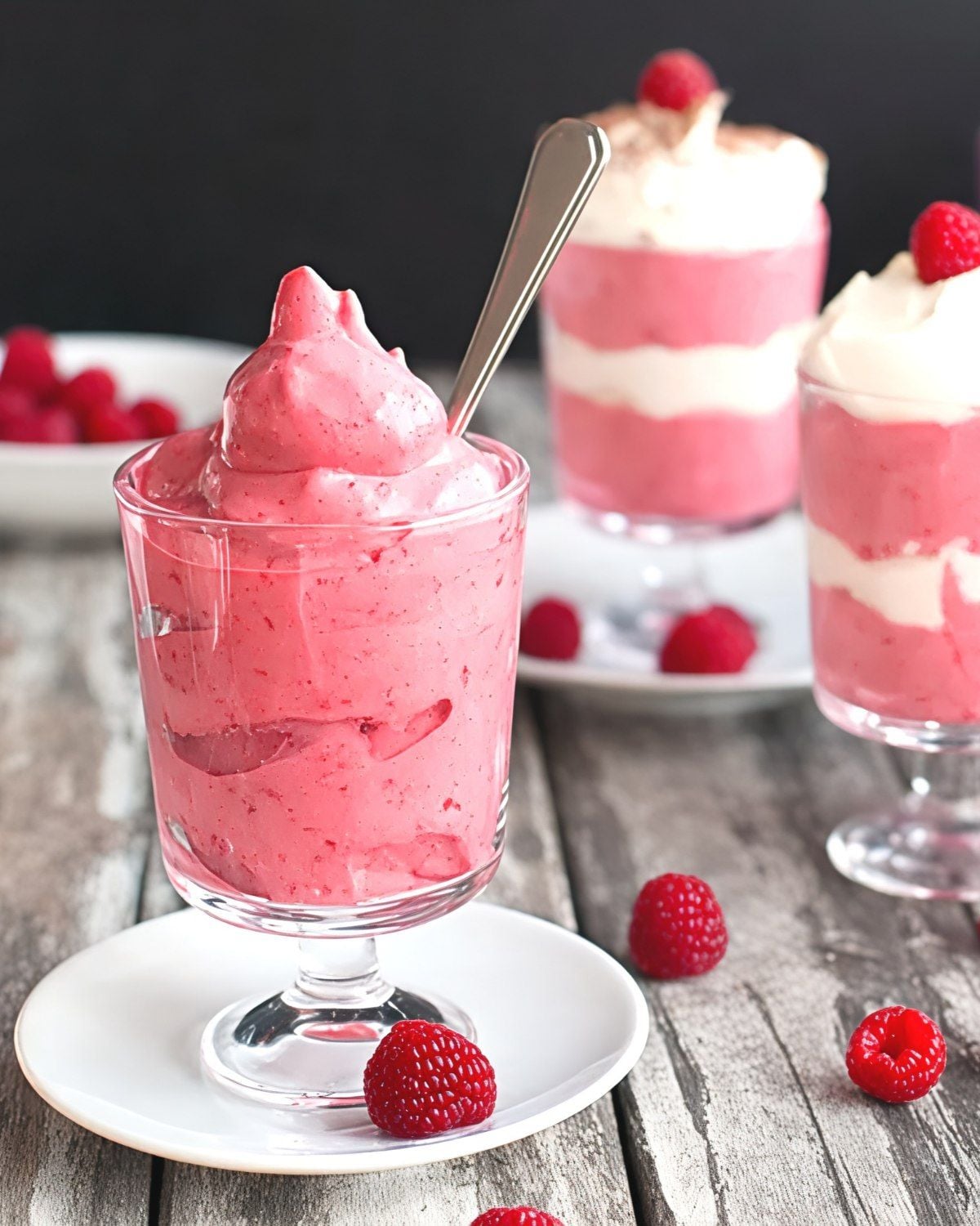 Creamy pink raspberry fruit mousse served in clear glass cups and garnished with fresh raspberries as an easy Thanksgiving dessert