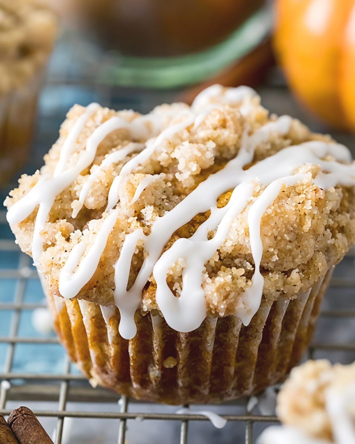 Soft pumpkin muffin topped with a streusel crumb topping and sweet white icing drizzle sitting on a wire rack for an easy Thanksgiving dessert.   