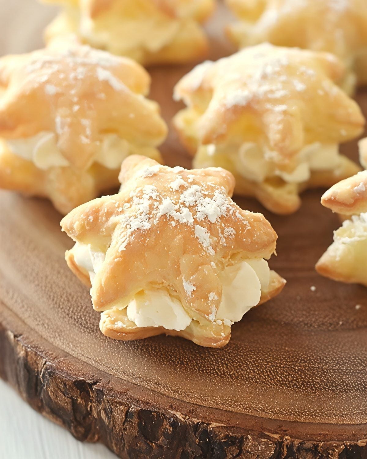 Golden star-shaped cream puffs filled with whipped cream and dusted with powdered sugar served on a wooden platter for an easy Thanksgiving dessert.