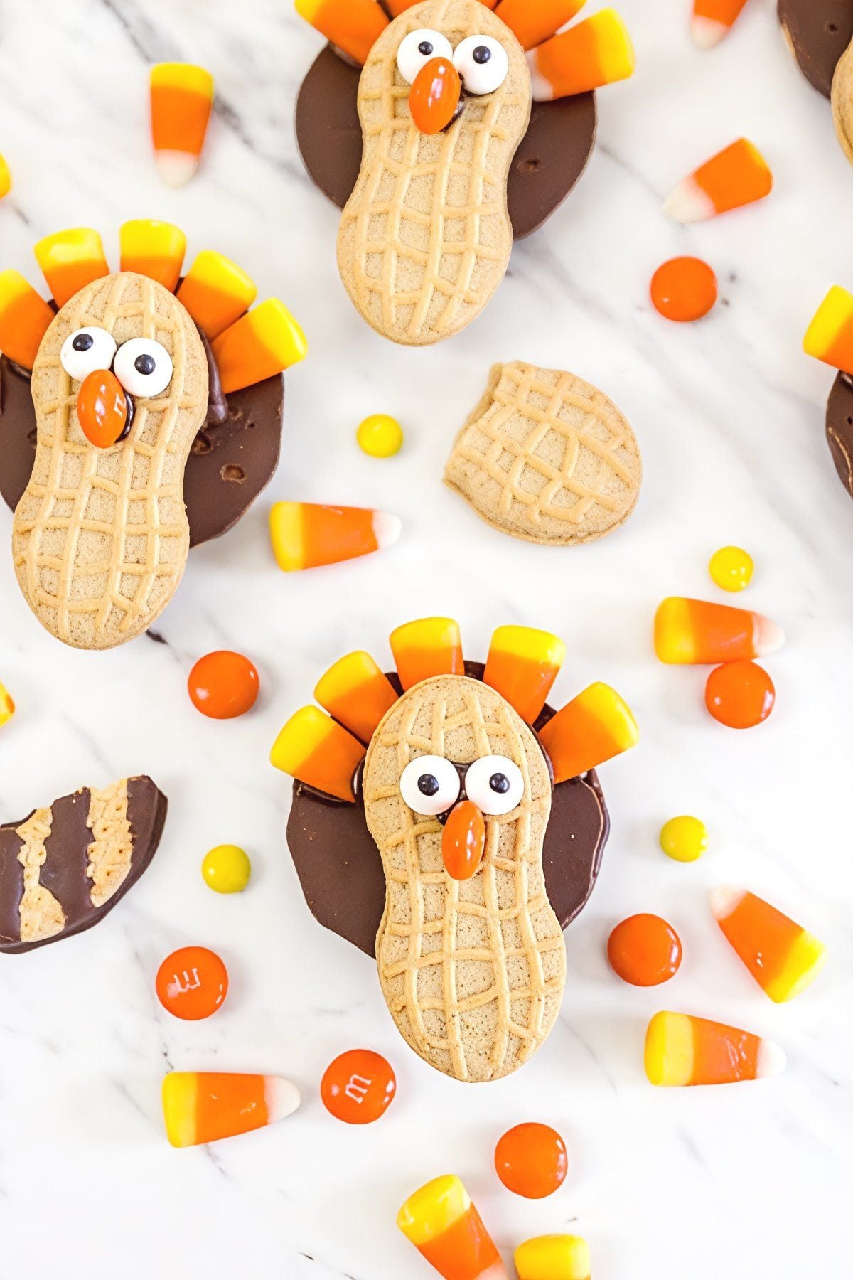 Fun Fudge Stripe turkey cookies made with Nutter Butter cookies, candy corn feathers, and candy eyes arranged on a marble surface for easy Thanksgiving desserts.