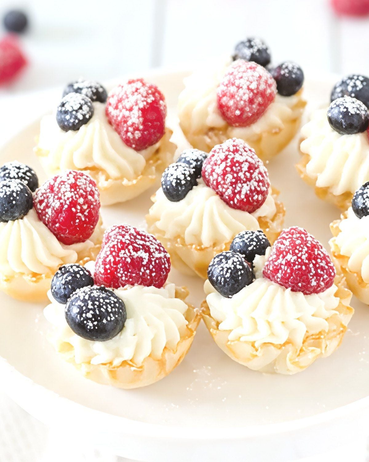 Creamy no-bake cheesecake bites in crispy pastry shells topped with fresh raspberries, blueberries, and powdered sugar for an easy Thanksgiving dessert.
