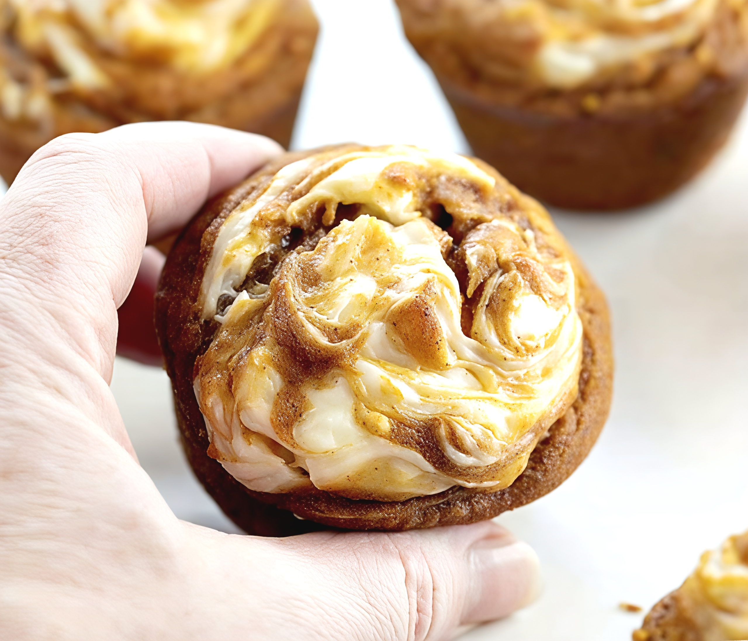 A hand holding a freshly baked pumpkin muffin swirled with sweet cream cheese on top for an easy Thanksgiving dessert.