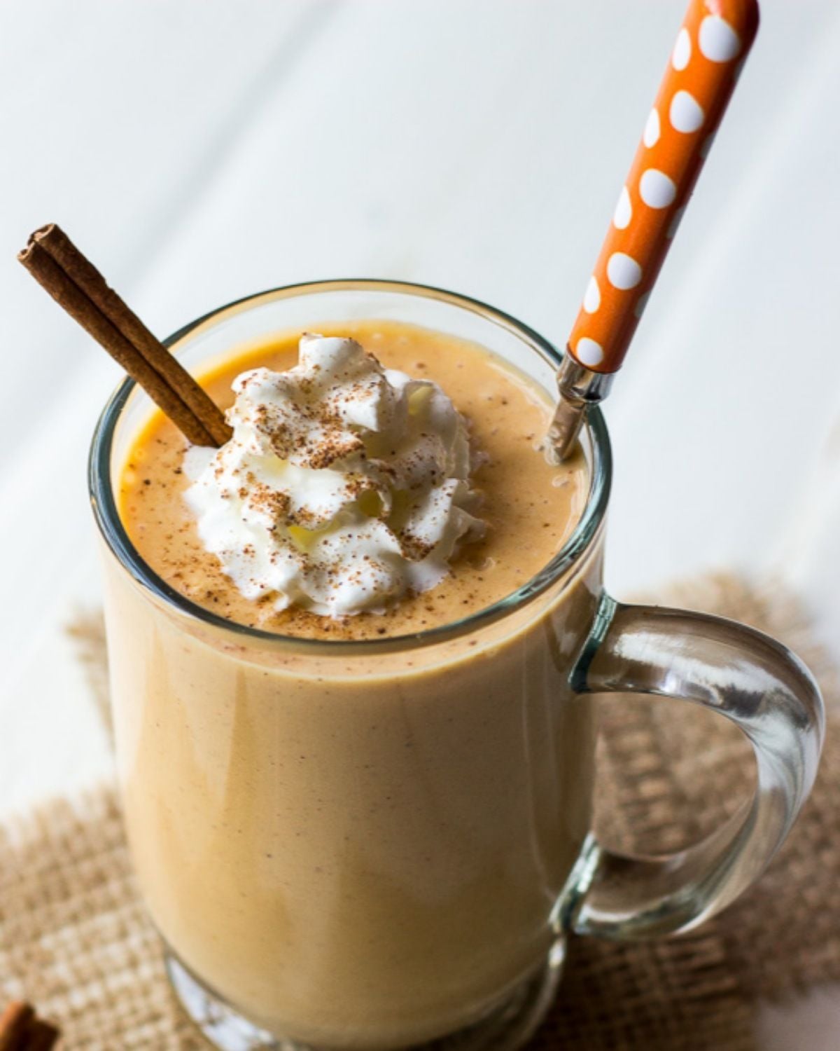 Creamy pumpkin pie smoothie topped with whipped cream, ground spices, and a cinnamon stick served in a glass mug as an easy Thanksgiving dessert.