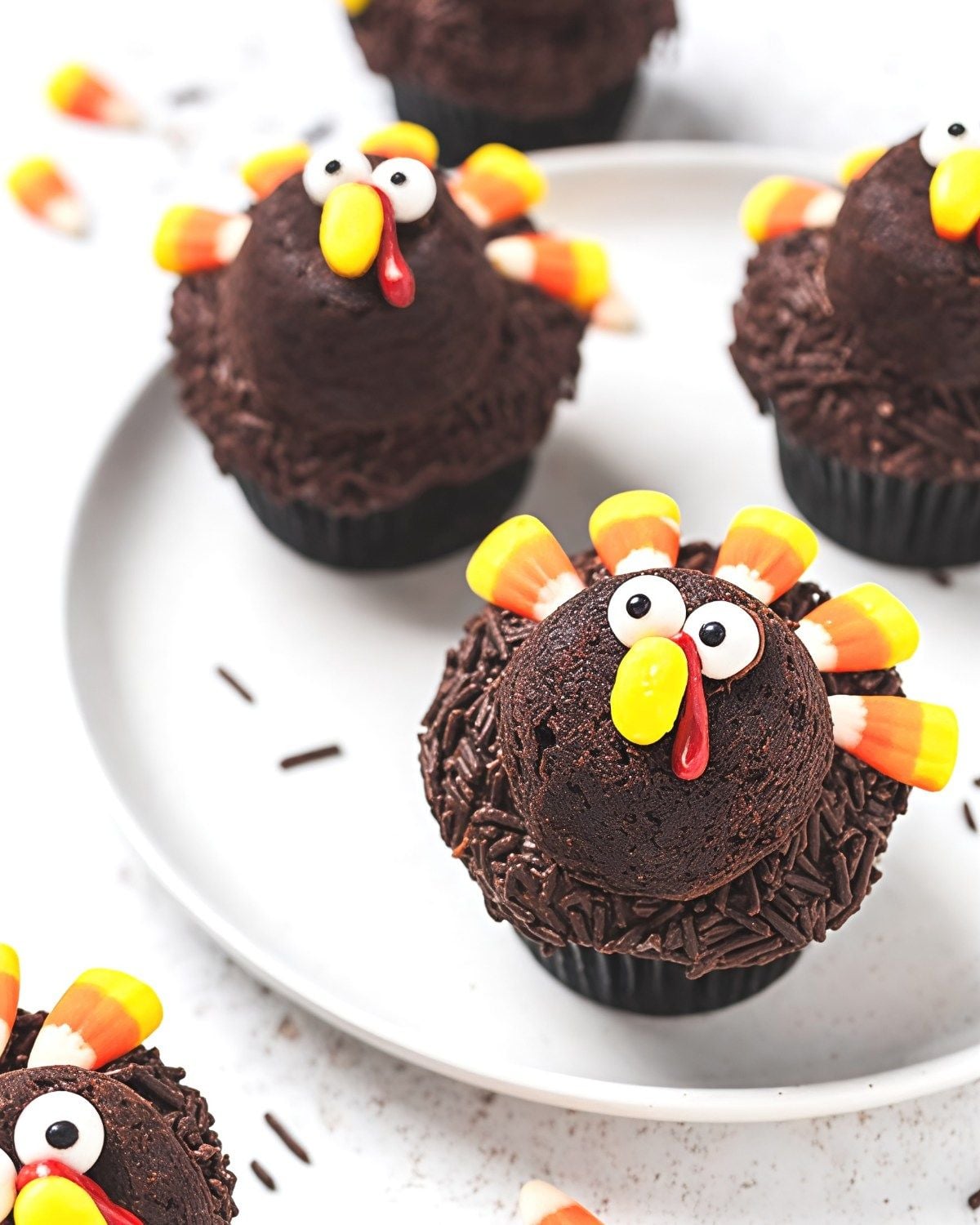 Festive Thanksgiving turkey cupcakes coated in chocolate sprinkles and decorated with candy corn feathers and candy eyes as an easy Thanksgiving dessert.