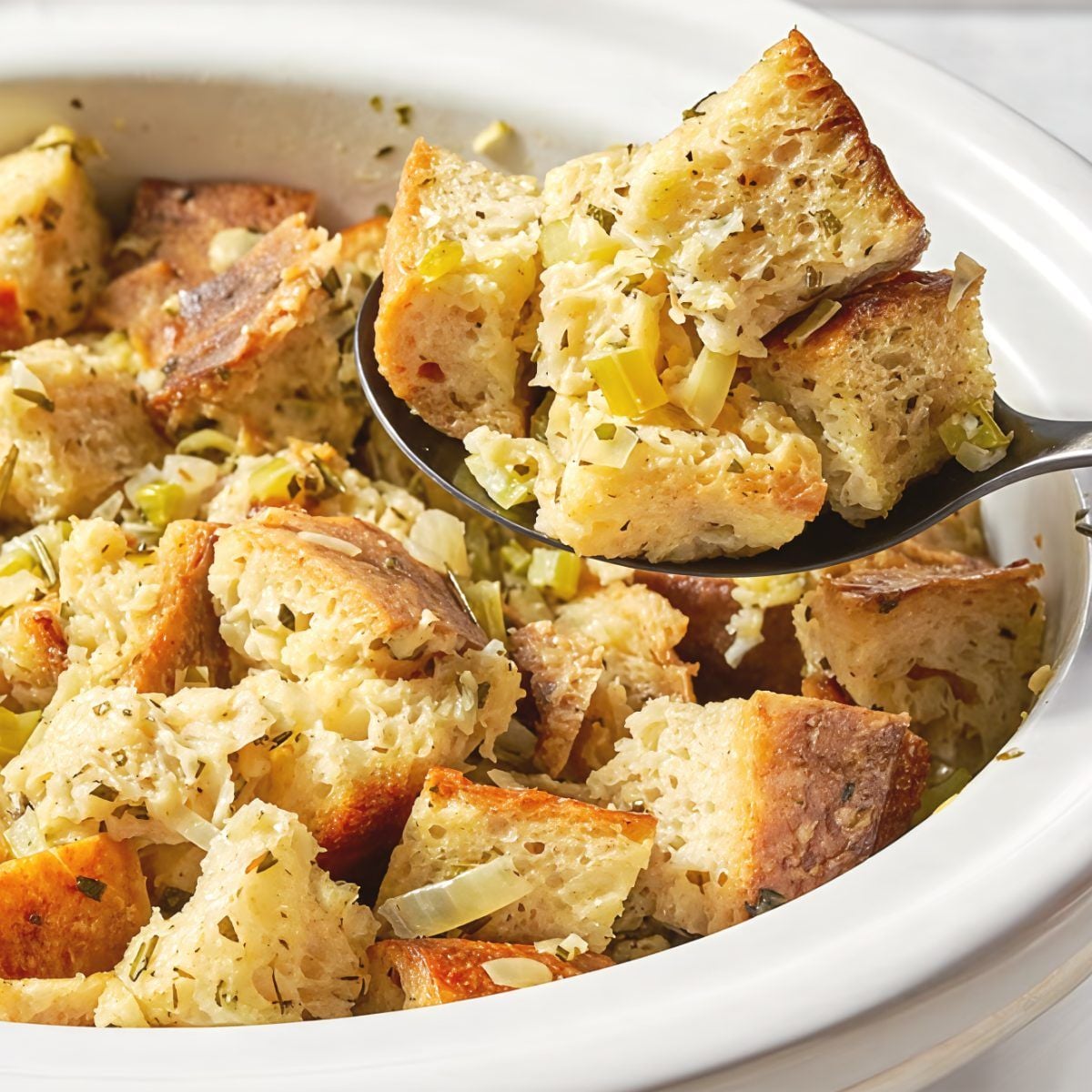 A serving spoon scooping warm crockpot stuffing thanksgiving recipe made with seasoned bread cubes, celery, and herbs from a slow cooker.