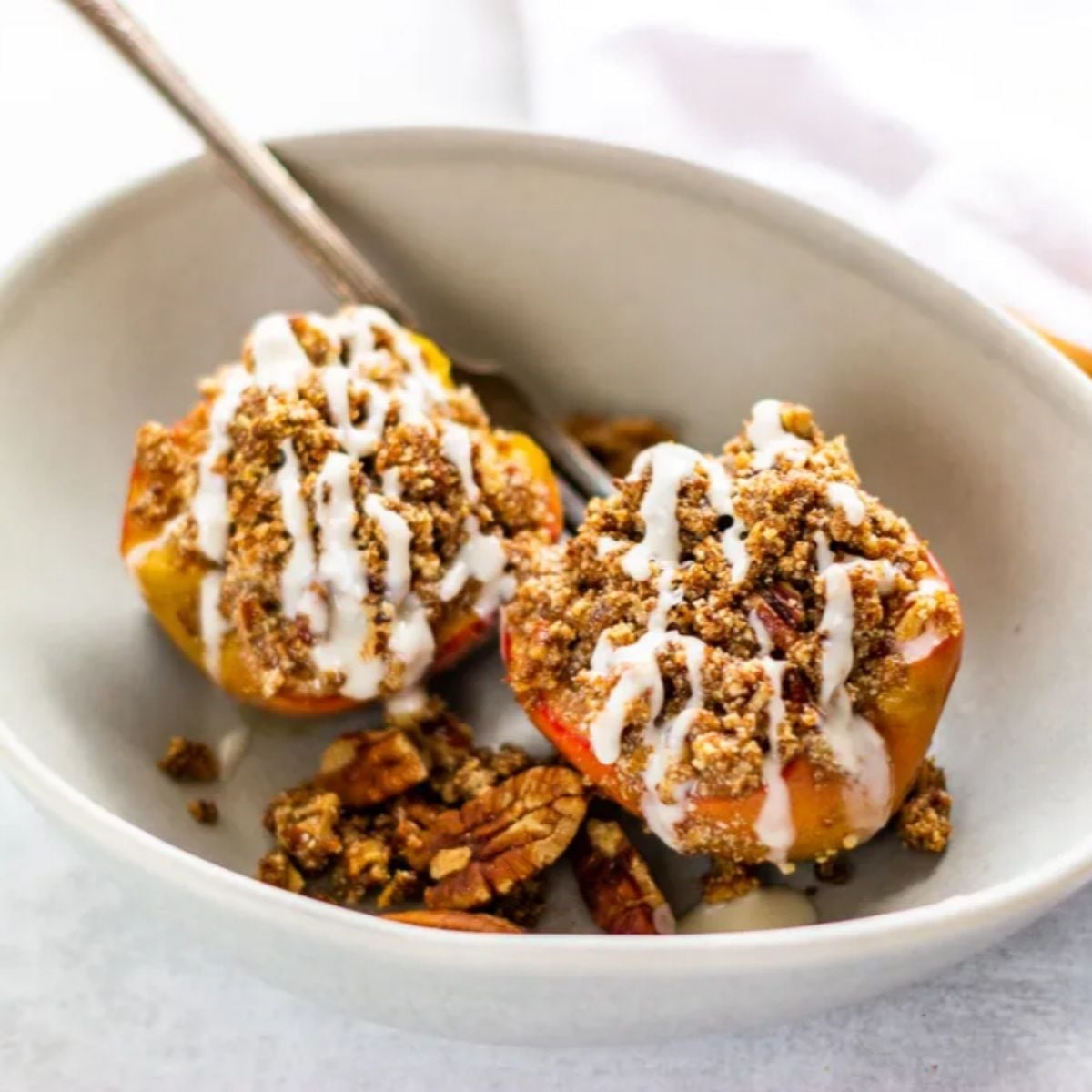 Paleo cinnamon crumble baked apples topped with a white drizzle and pecans, perfect for gluten-free Thanksgiving desserts.