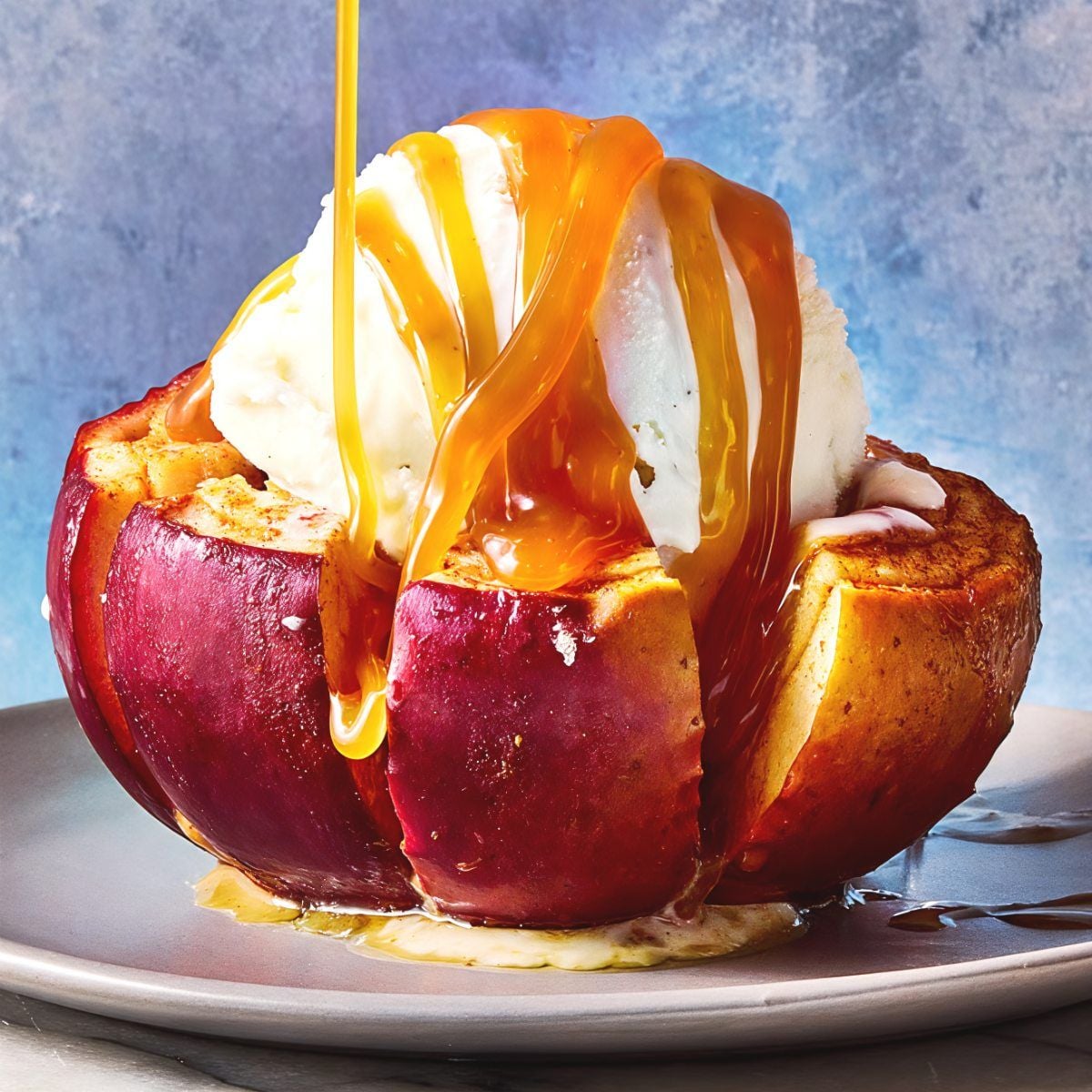 A sliced blooming baked apple topped with a scoop of vanilla ice cream and warm caramel drizzle, perfect for gluten-free Thanksgiving desserts.