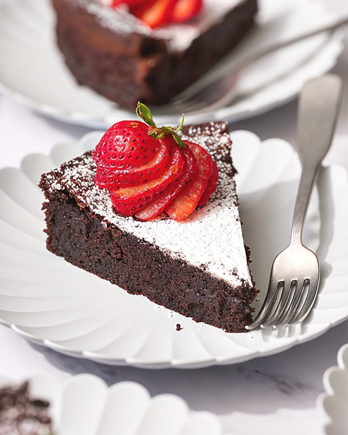 A slice of rich flourless chocolate cake dusted with powdered sugar and topped with fresh strawberries, perfect for gluten-free Thanksgiving desserts.