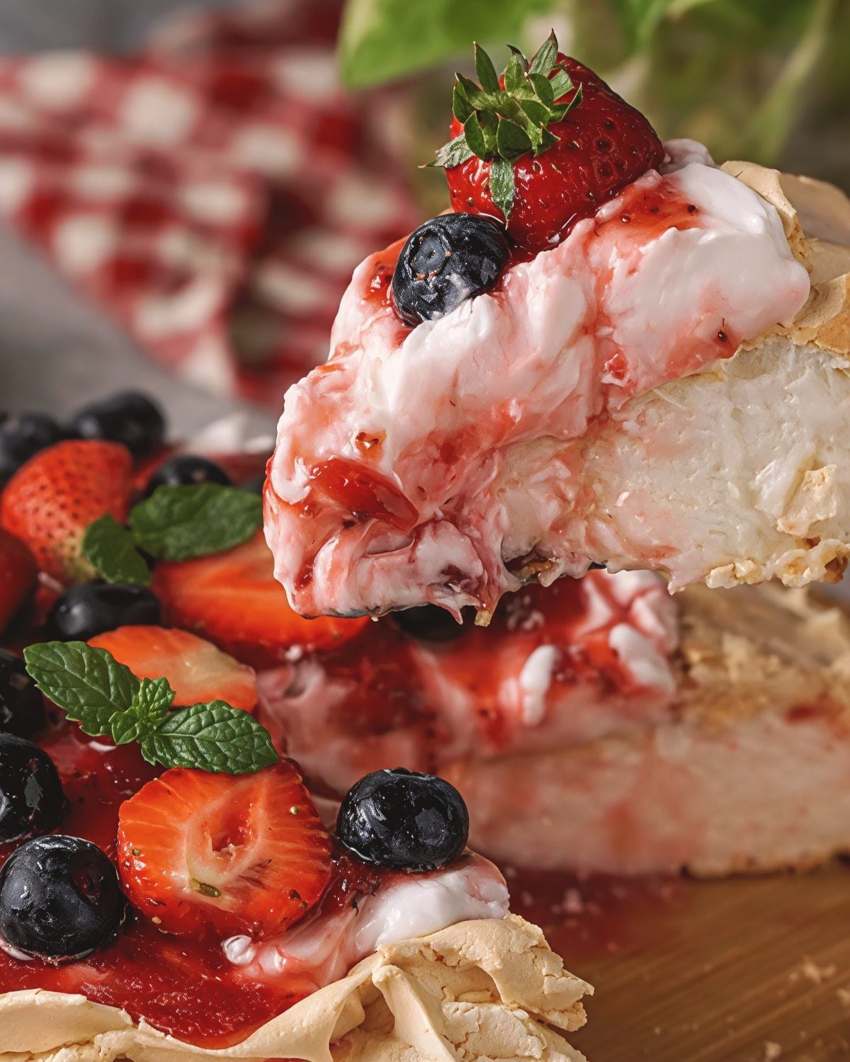 A slice of crisp meringue pavlova topped with whipped cream, fresh strawberries, blueberries, and berry sauce, ideal for gluten-free Thanksgiving desserts.