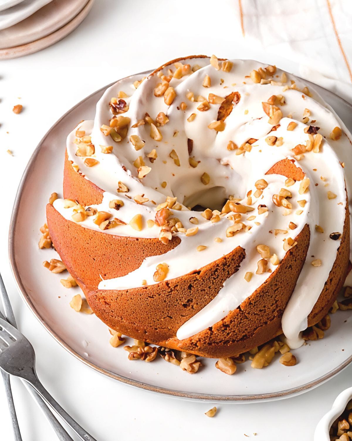 A delicious gluten-free pumpkin bundt cake topped with white icing and chopped walnuts, perfect for gluten-free Thanksgiving desserts.