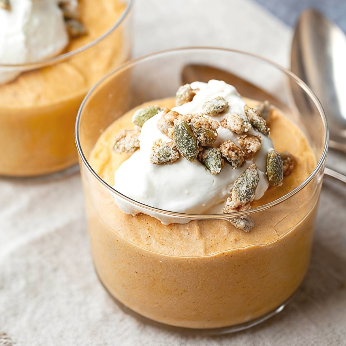 A glass cup of creamy gluten-free pumpkin mousse topped with whipped cream and candied pumpkin seeds, perfect for gluten-free Thanksgiving desserts
