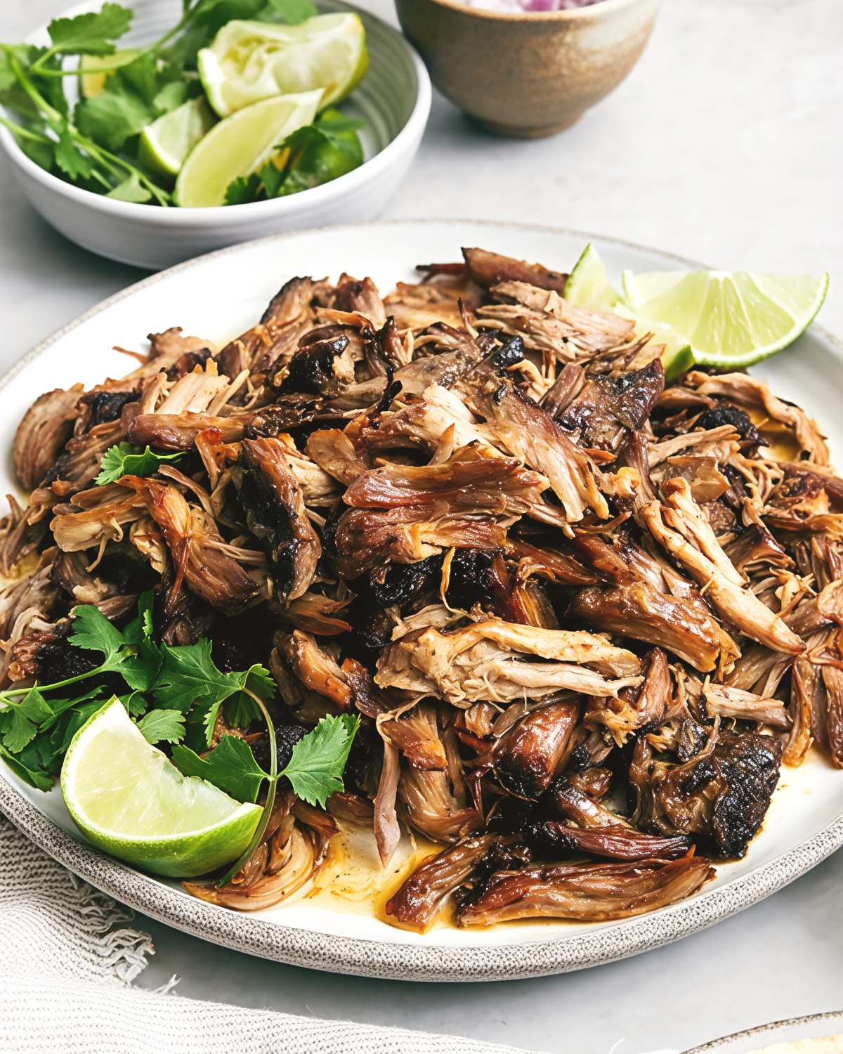 A platter of tender, crispy Mexican pork carnitas cooked in a slow cooker, garnished with fresh cilantro sprigs and lime wedges.