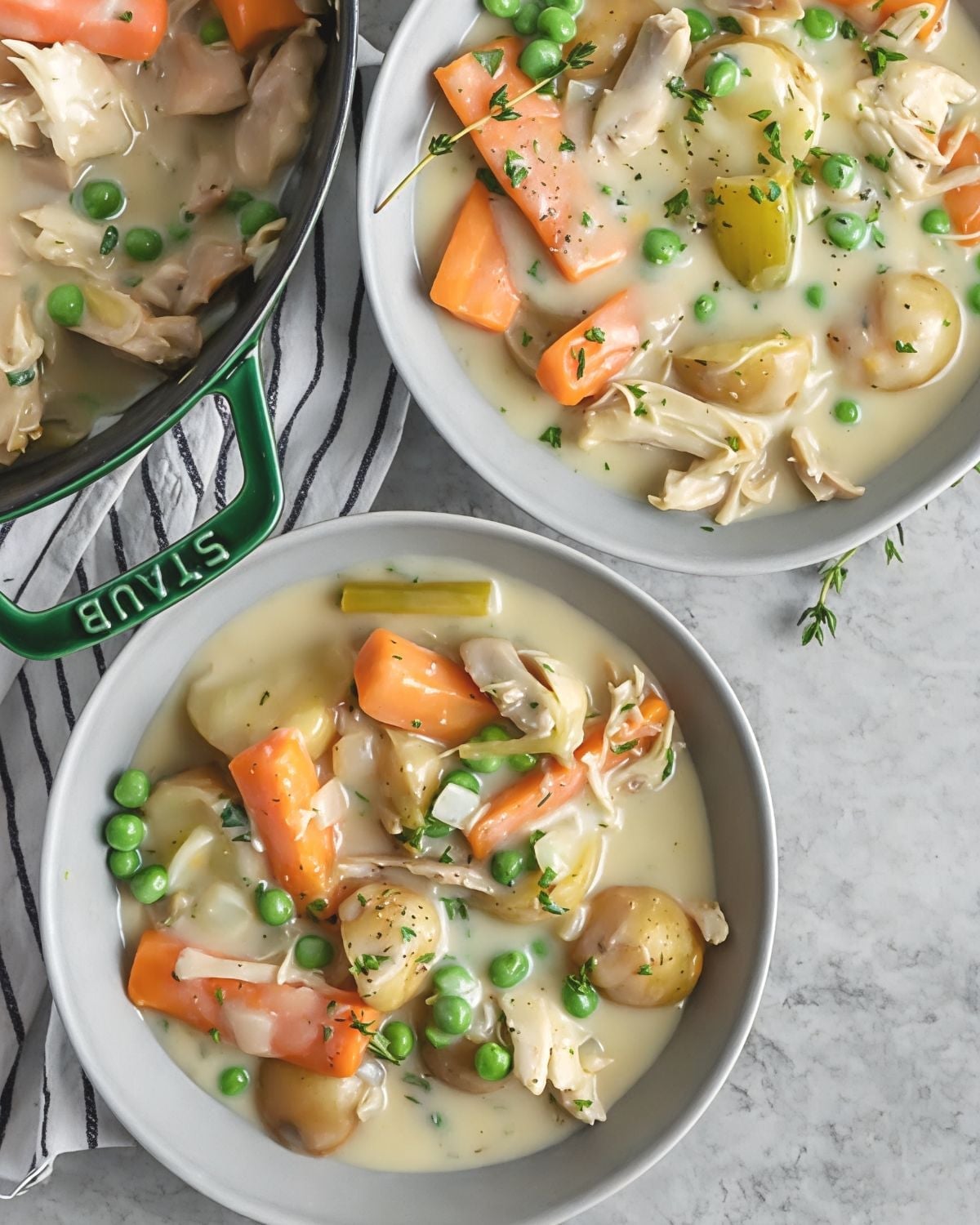 Two bowls filled with hearty leftover turkey stew loaded with tender shredded turkey, carrots, green peas, baby potatoes, and fresh thyme, served next to a Staub Dutch oven