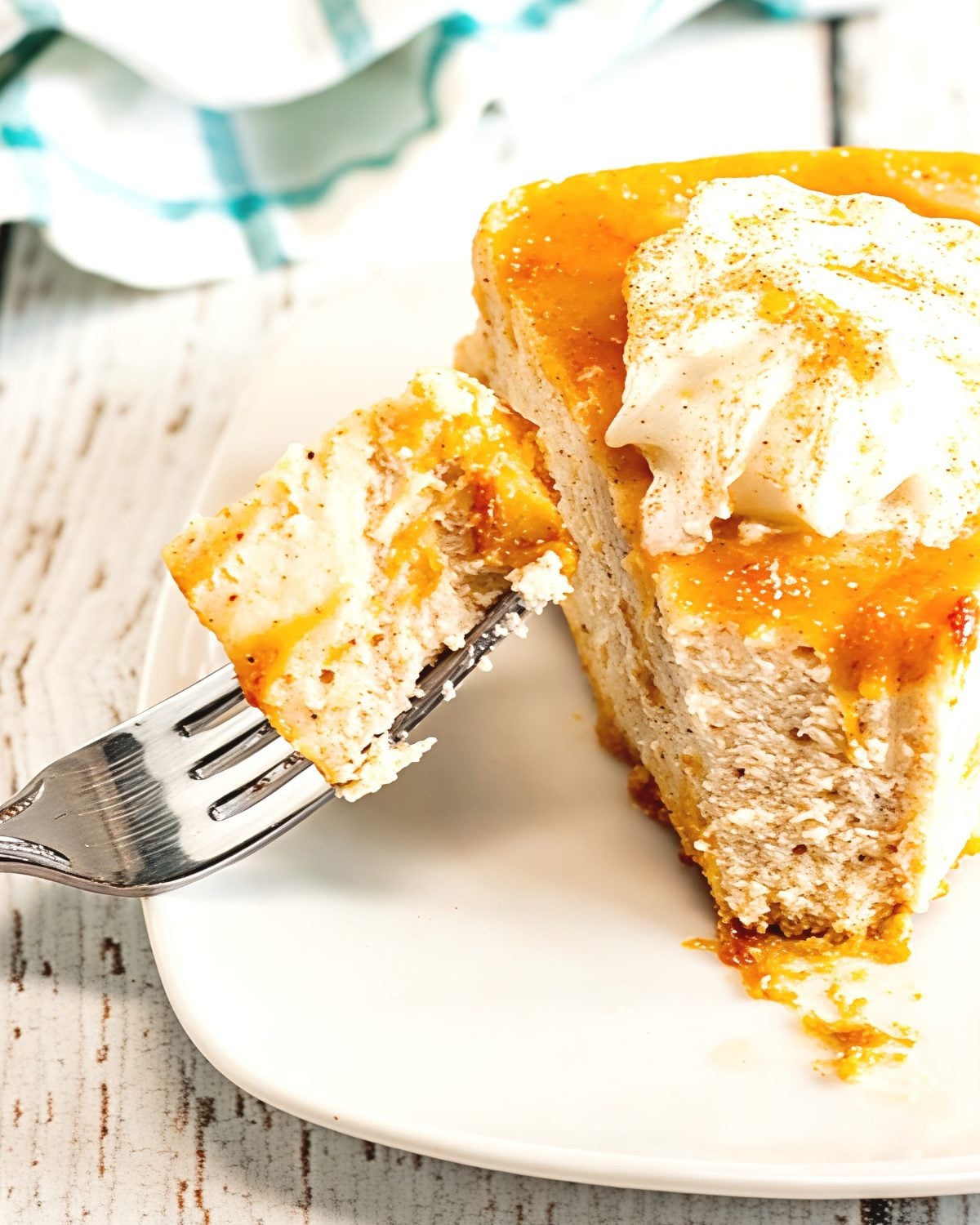 A slice of creamy Instant Pot eggnog cheesecake on a gingersnap crust, topped with caramel drizzle, whipped cream, and a dusting of nutmeg as a fork lifts a bite.
