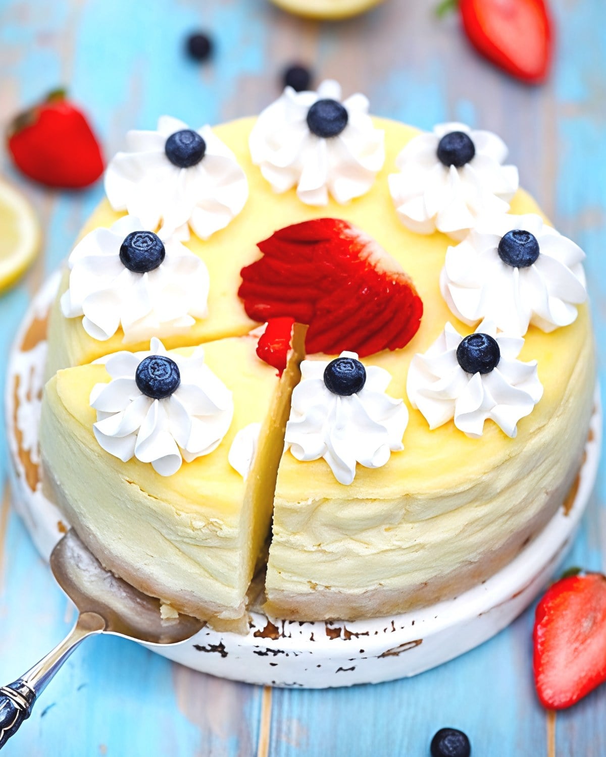 Round keto lemon cheesecake topped with whipped cream swirls, blueberries, and a red berry sauce center, perfect for Thanksgiving dessert ideas.