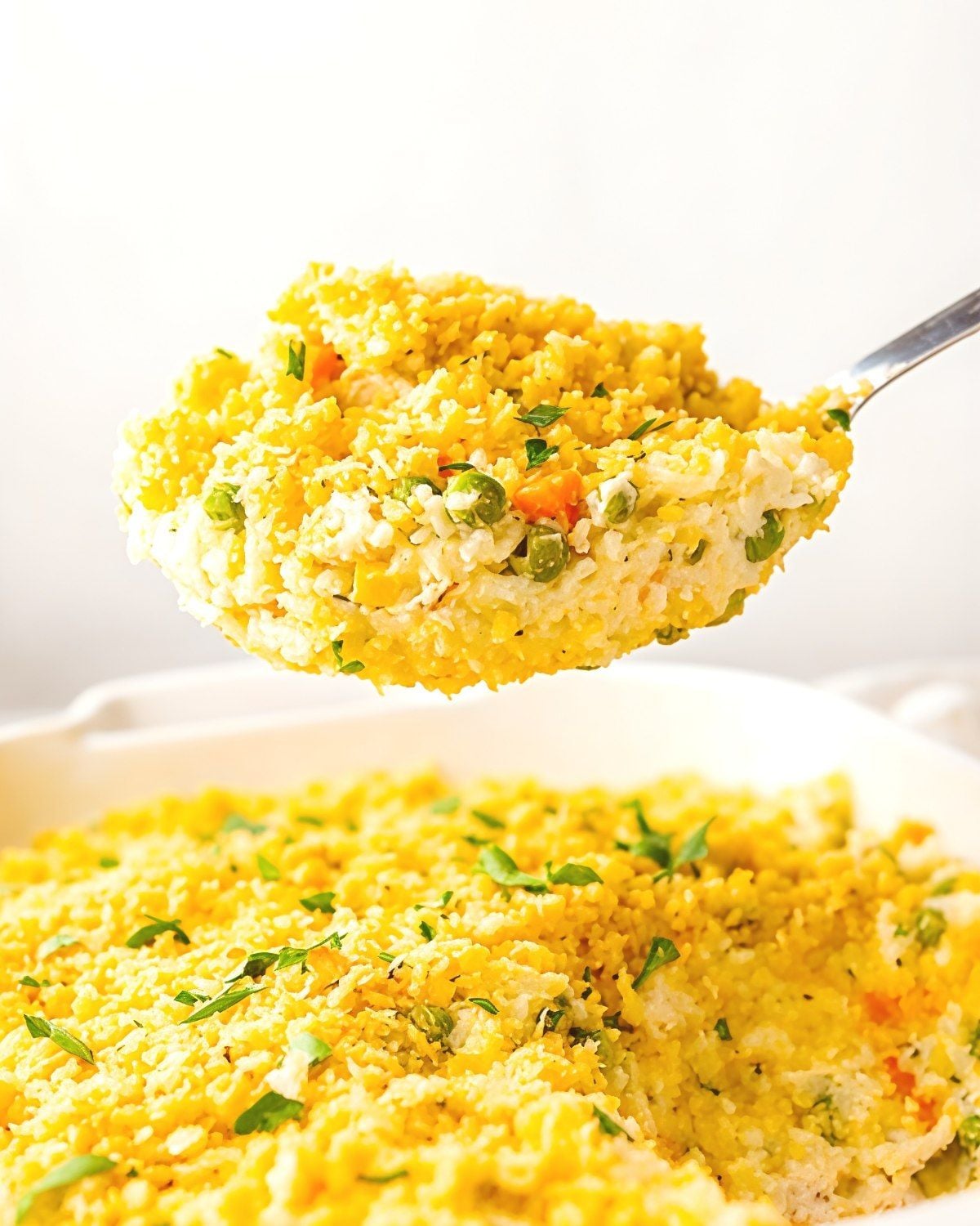 A serving spoon scooping cheesy Instant Pot turkey and rice casserole mixed with peas and carrots out of a baking dish.