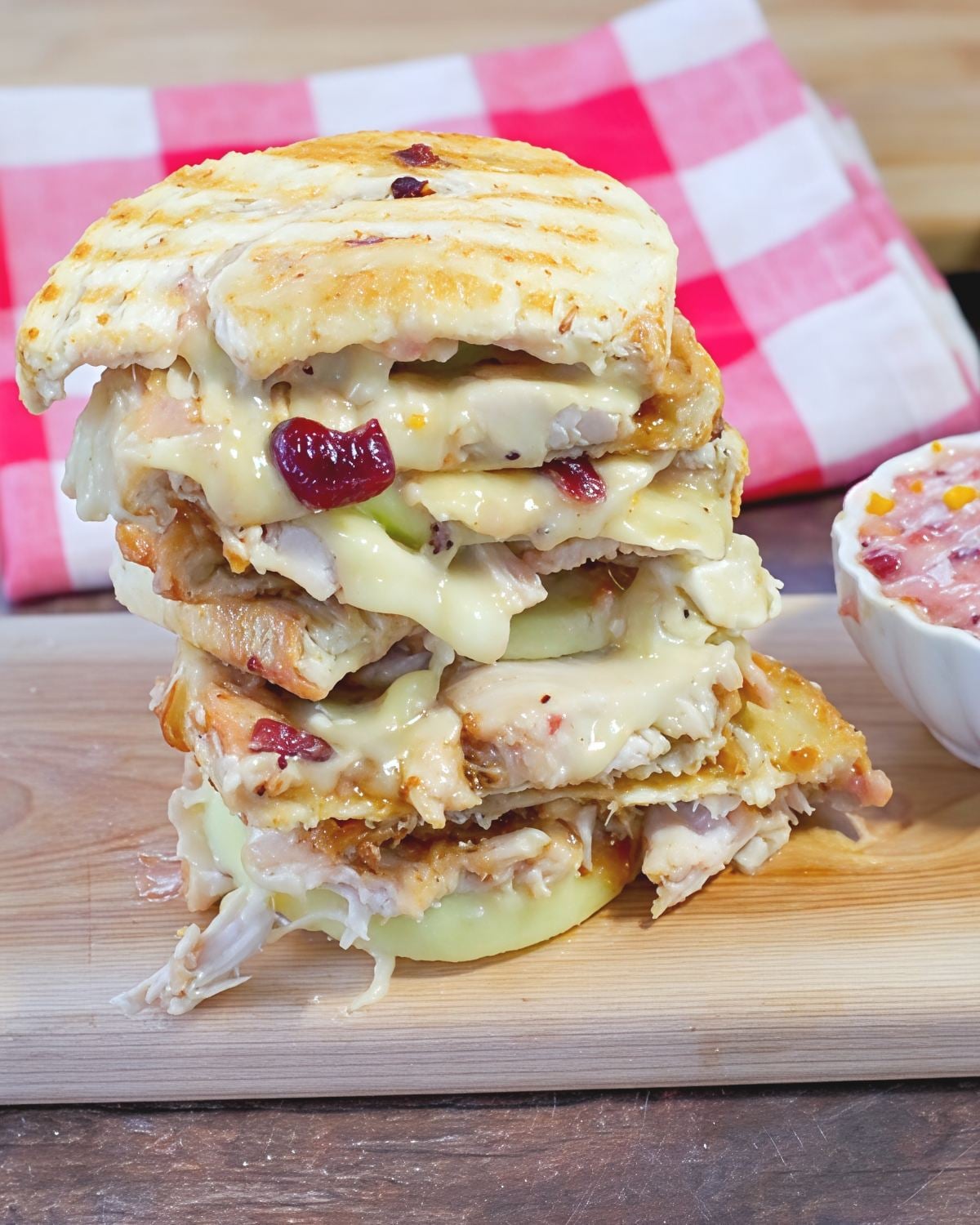 Crispy grilled leftover turkey breast panini stacked high with gooey melted Brie cheese, crisp apple slices, and cranberry sauce on a wooden cutting board.