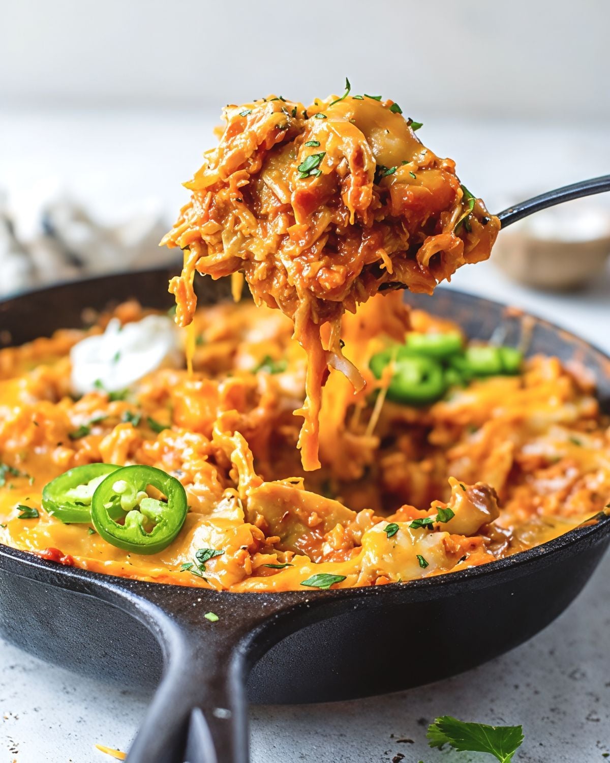 Cheesy leftover turkey breast enchilada skillet topped with fresh jalapeños and being scooped from a cast iron pan.