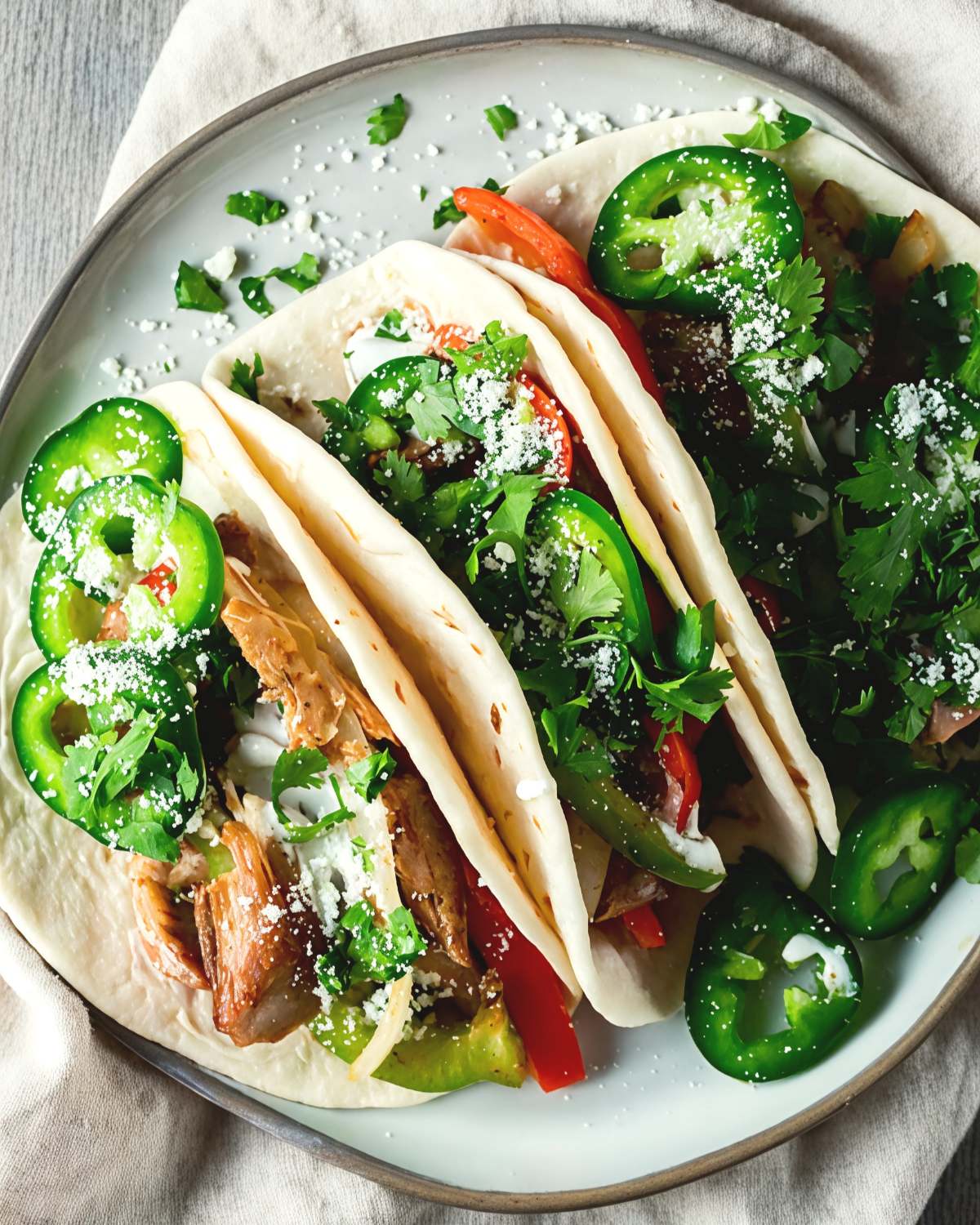 Sizzling leftover turkey breast fajitas stuffed into warm flour tortillas with bell peppers, fresh jalapeño slices, cilantro, and cotija cheese on a serving plate.