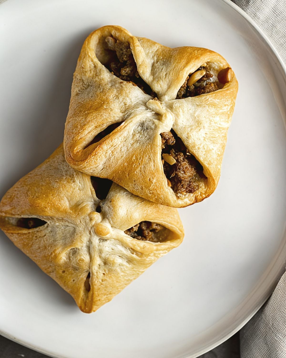 Golden-brown baked leftover turkey breast hand pies filled with seasoned turkey stuffing arranged on a white plate.