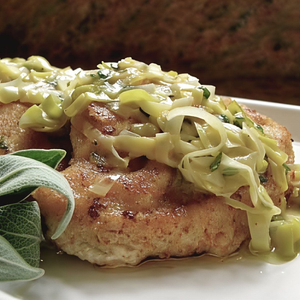 Sautéed leftover turkey breast topped with tender leeks and a buttery sage sauce, garnished with fresh sage leaves on a serving plate.