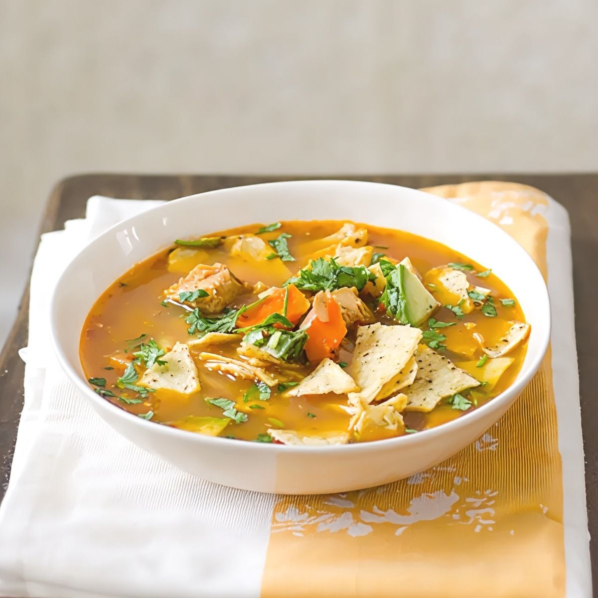 Hearty leftover turkey breast tortilla soup topped with crispy tortilla chips, avocado, and cilantro in a white bowl.