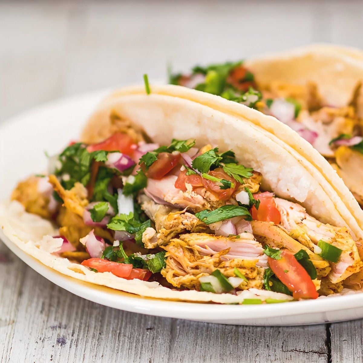 Soft tacos stuffed with shredded leftover turkey carnitas and topped with fresh pico de gallo salsa, diced red onions, and cilantro on a white plate.