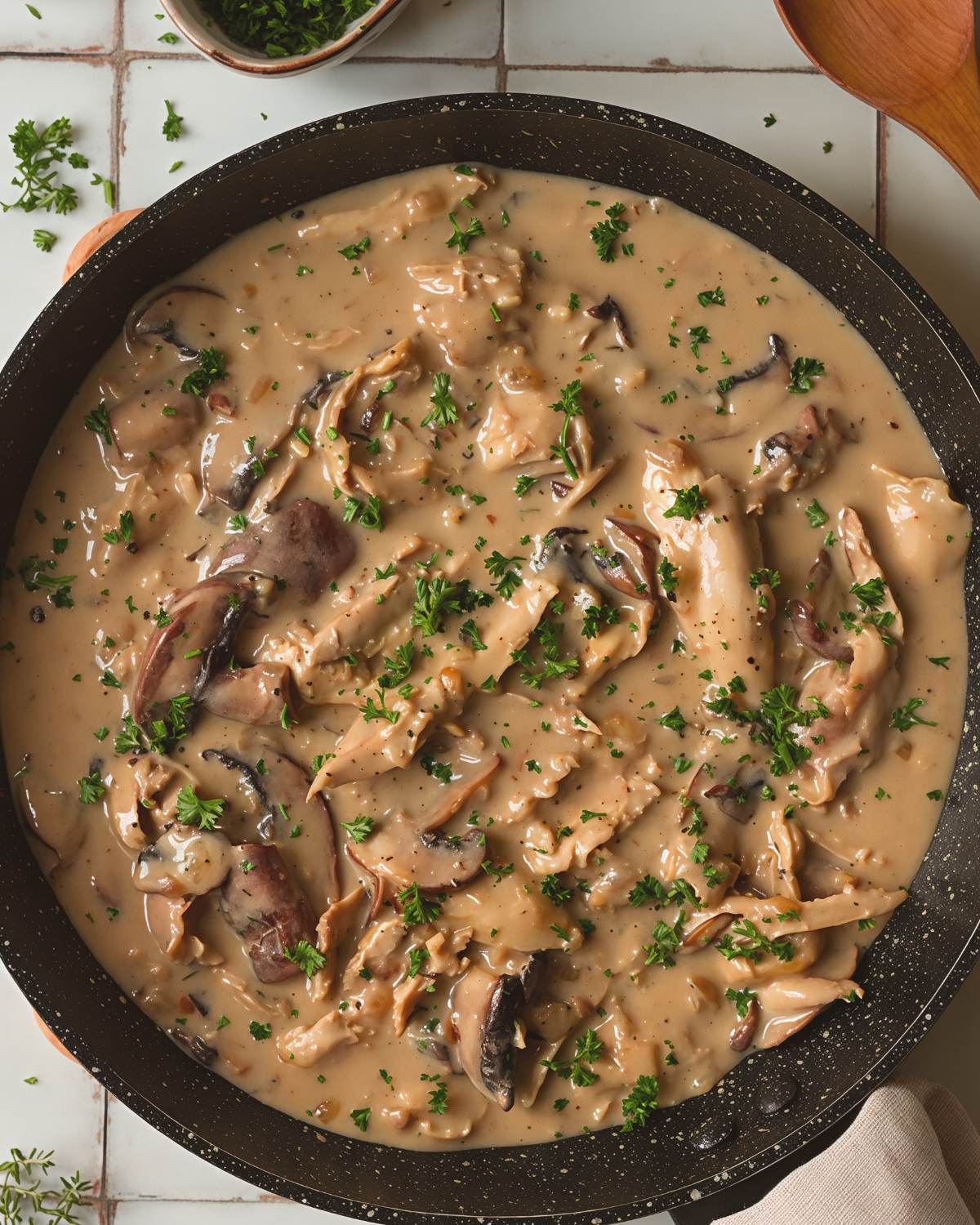 Creamy leftover turkey fricassee with sliced mushrooms and fresh parsley simmering in a skillet.