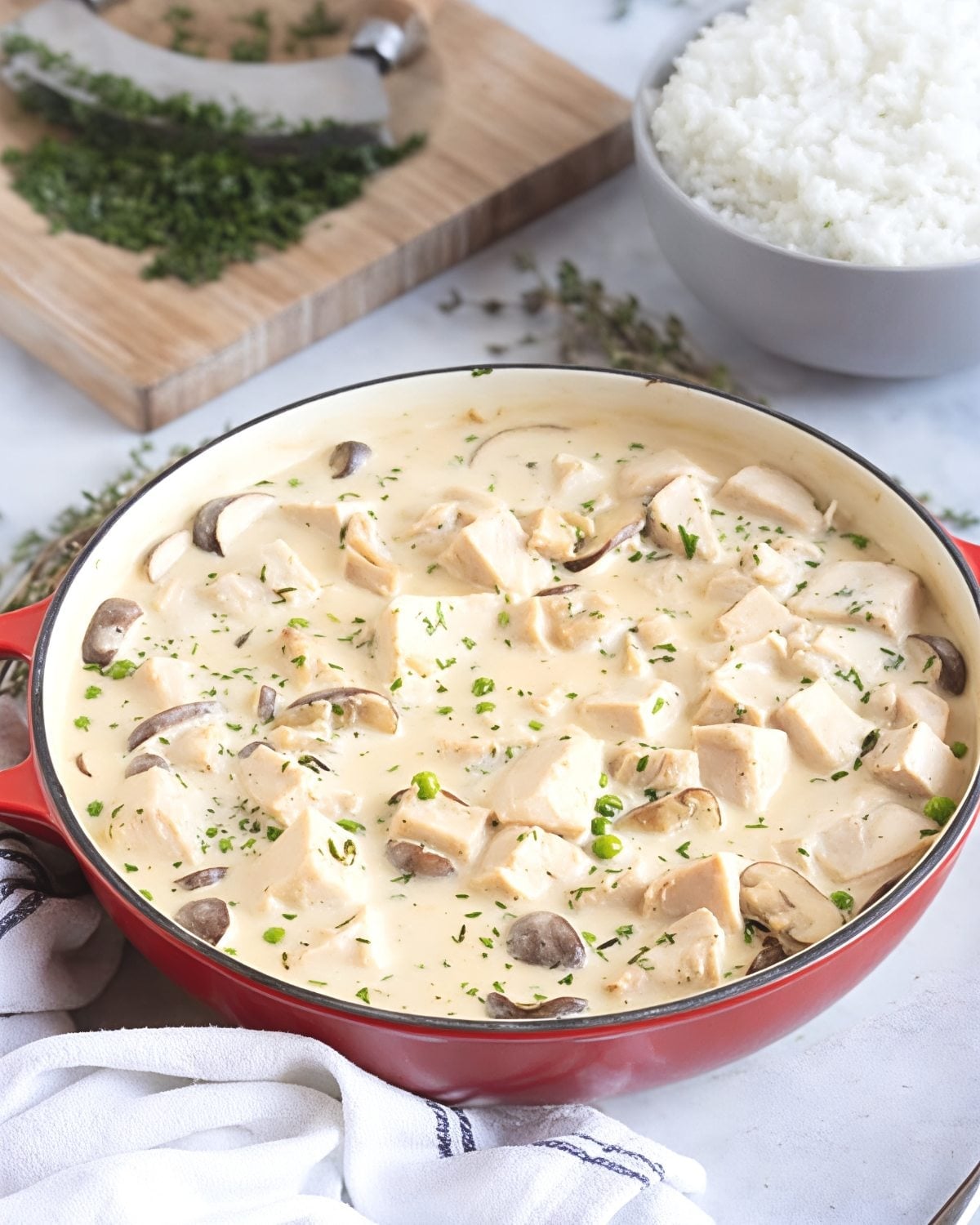 A red skillet filled with rich and creamy turkey fricassee featuring tender diced leftover turkey, sliced mushrooms, and fresh herbs, served alongside a bowl of white rice.