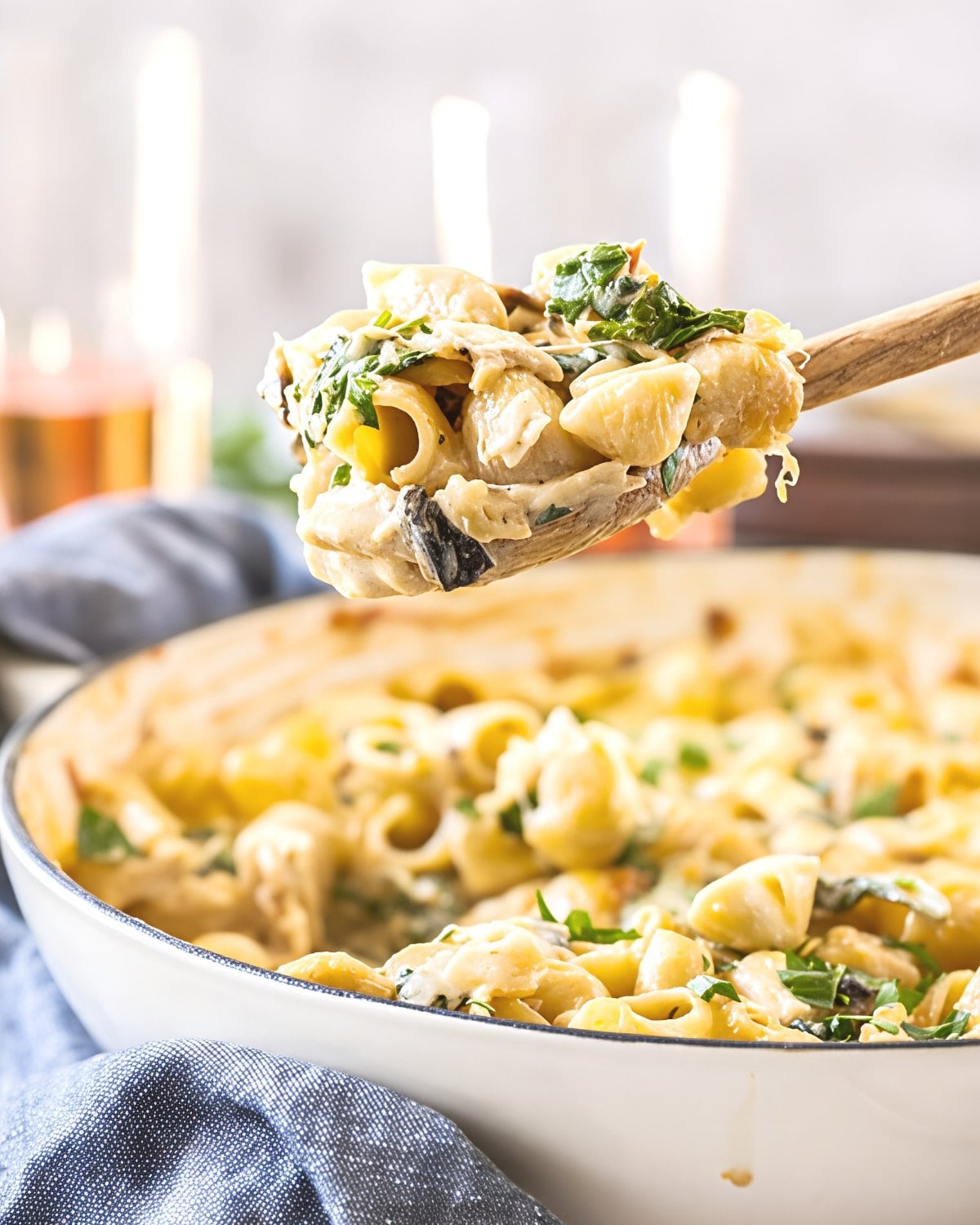 A wooden spoon scooping creamy leftover turkey pasta bake loaded with shell pasta, spinach, and mushrooms from a casserole dish.