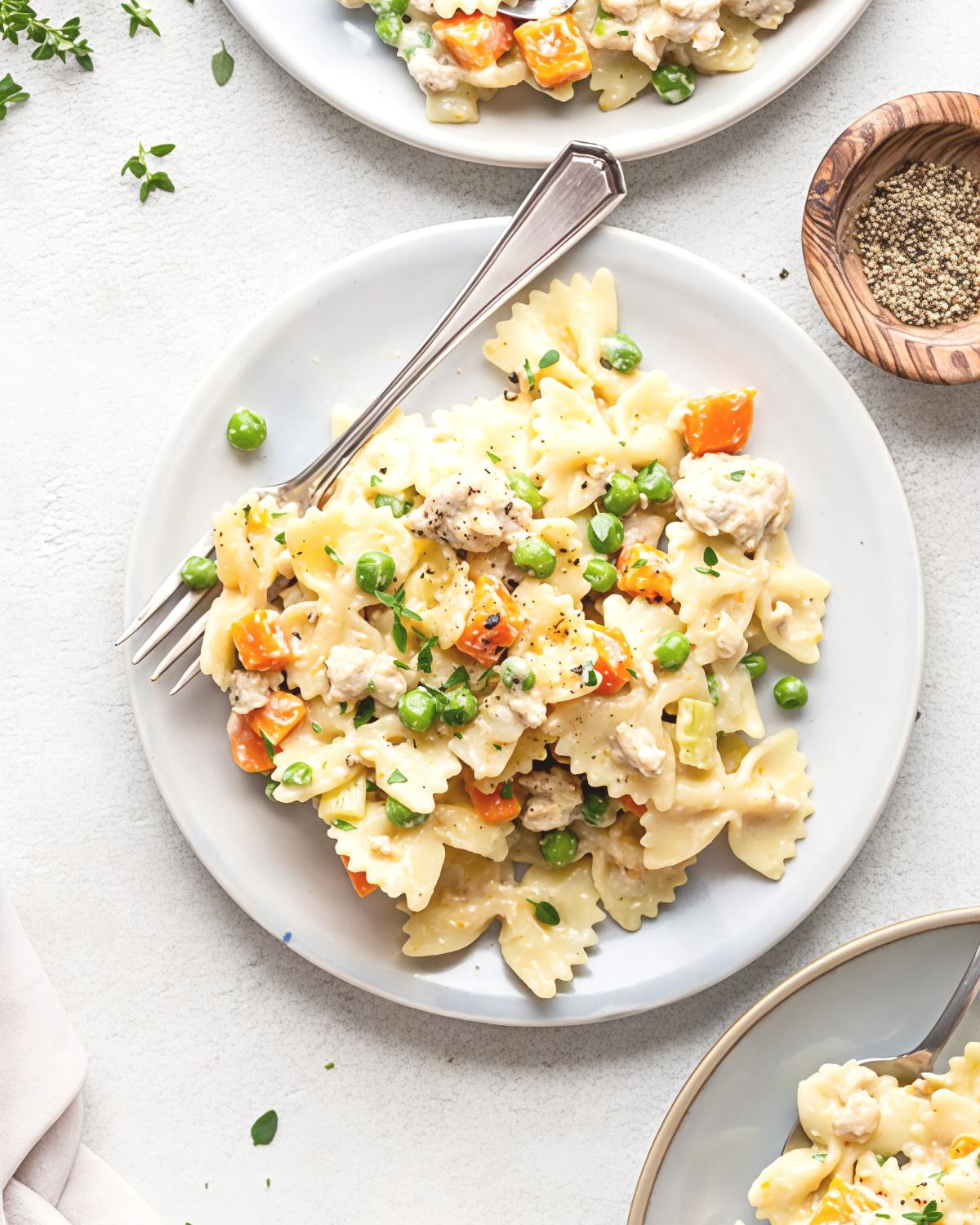 A plate of creamy bow tie pasta tossed with leftover turkey, tender carrots, green peas, fresh herbs, and cracked black pepper.