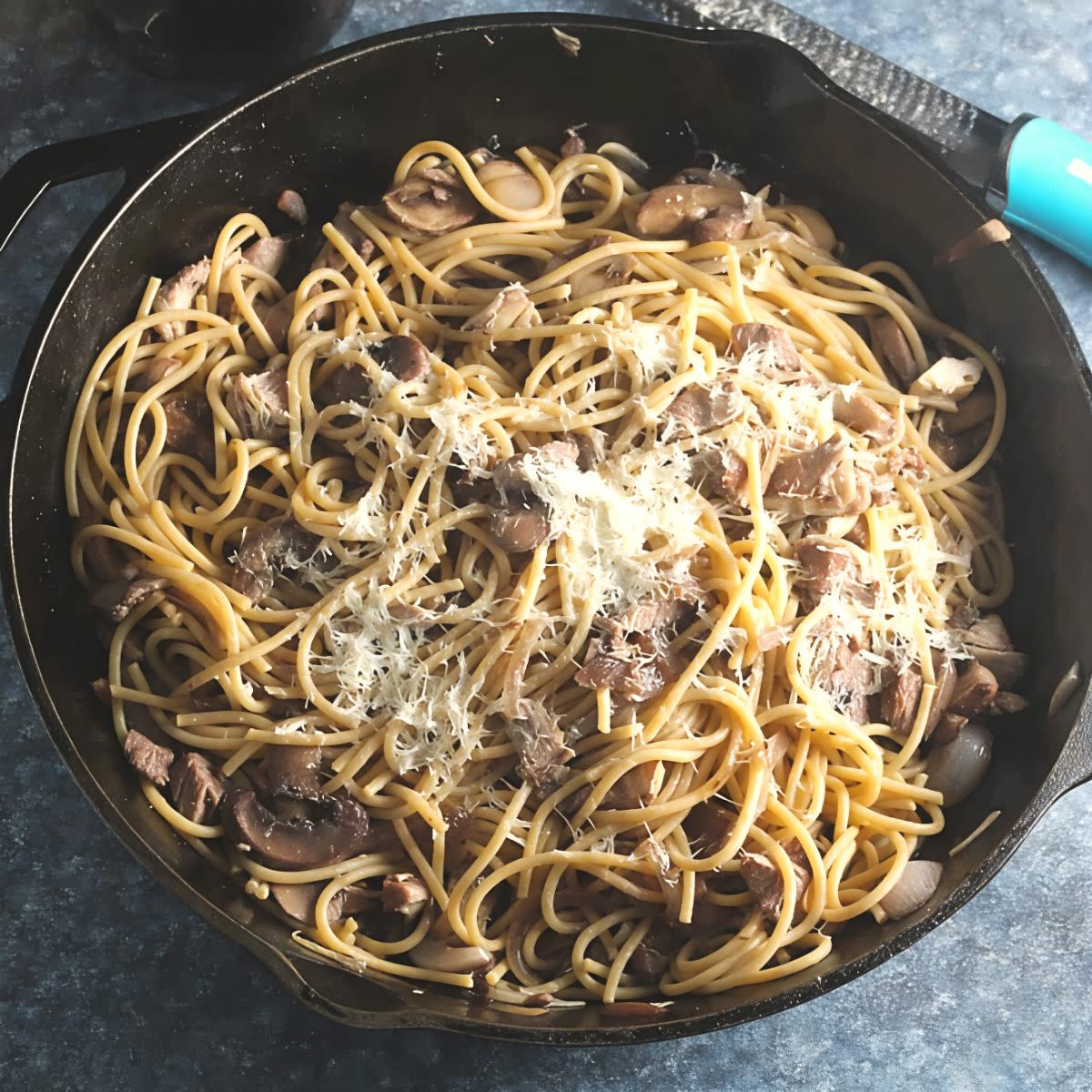 Savory leftover turkey pasta tossed with sautéed mushrooms and grated Parmesan cheese served in a cast-iron skillet.