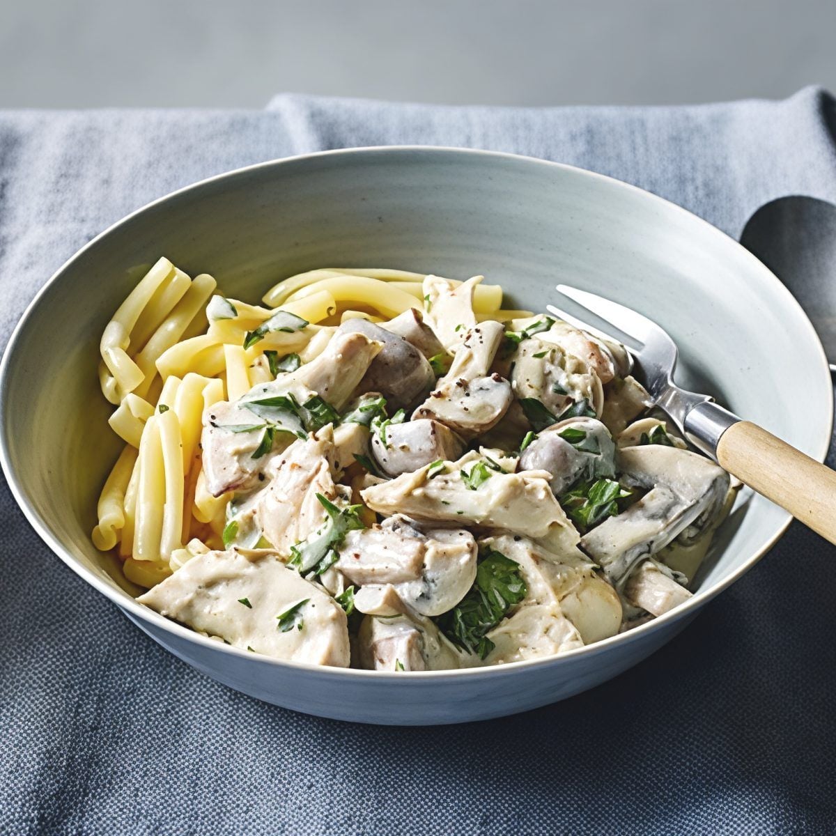 Creamy leftover turkey fricassee with mushrooms and fresh herbs served alongside tender pasta in a grey bowl, perfect for easy leftover turkey recipes.