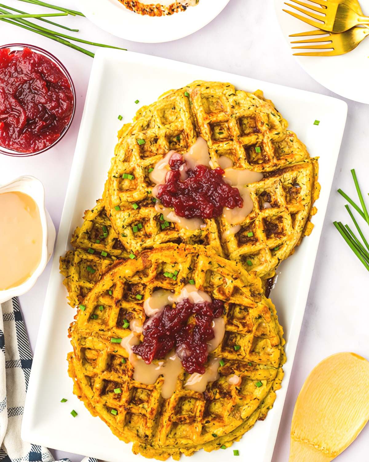 Crispy savory leftover stuffing waffles topped with warm turkey gravy and cranberry sauce on a white platter, ideal for creative leftover turkey recipes.