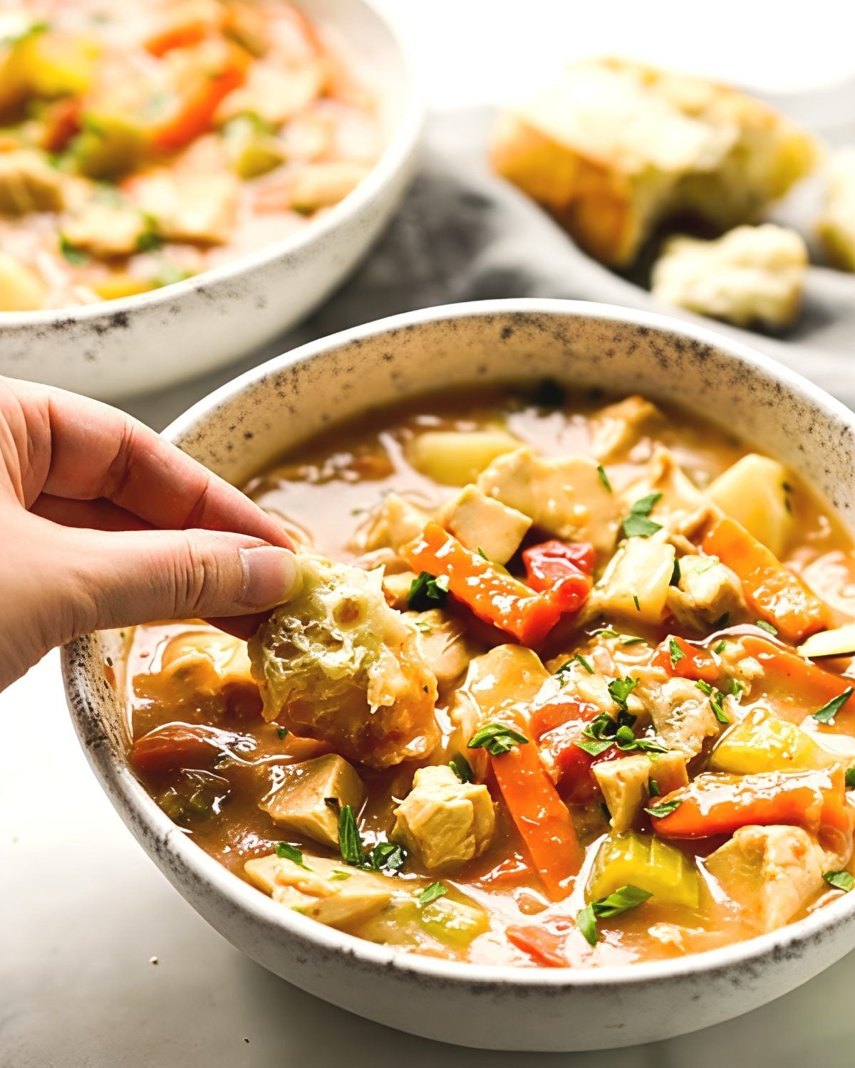 Hearty leftover turkey stew with tender vegetables in a bowl being dipped with crusty bread, perfect for delicious leftover turkey recipes.