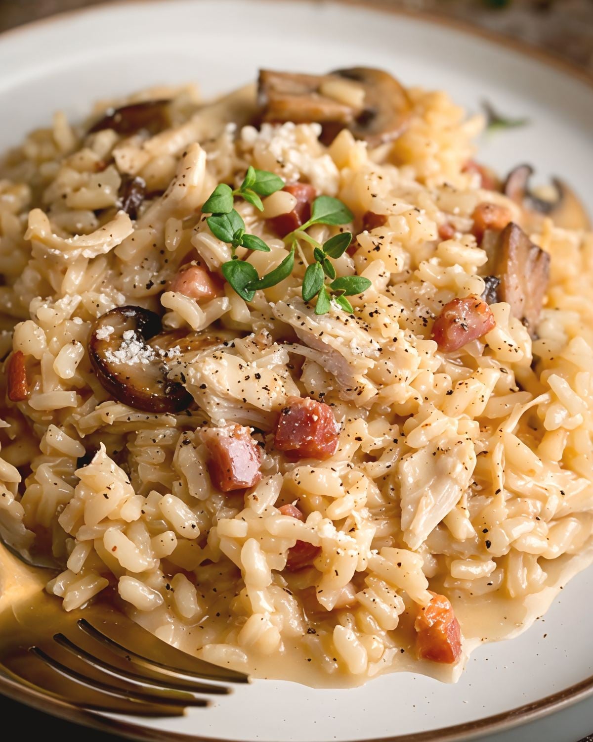Creamy leftover turkey risotto stirred with sliced mushrooms and pancetta, garnished with fresh thyme leaves on a white plate.