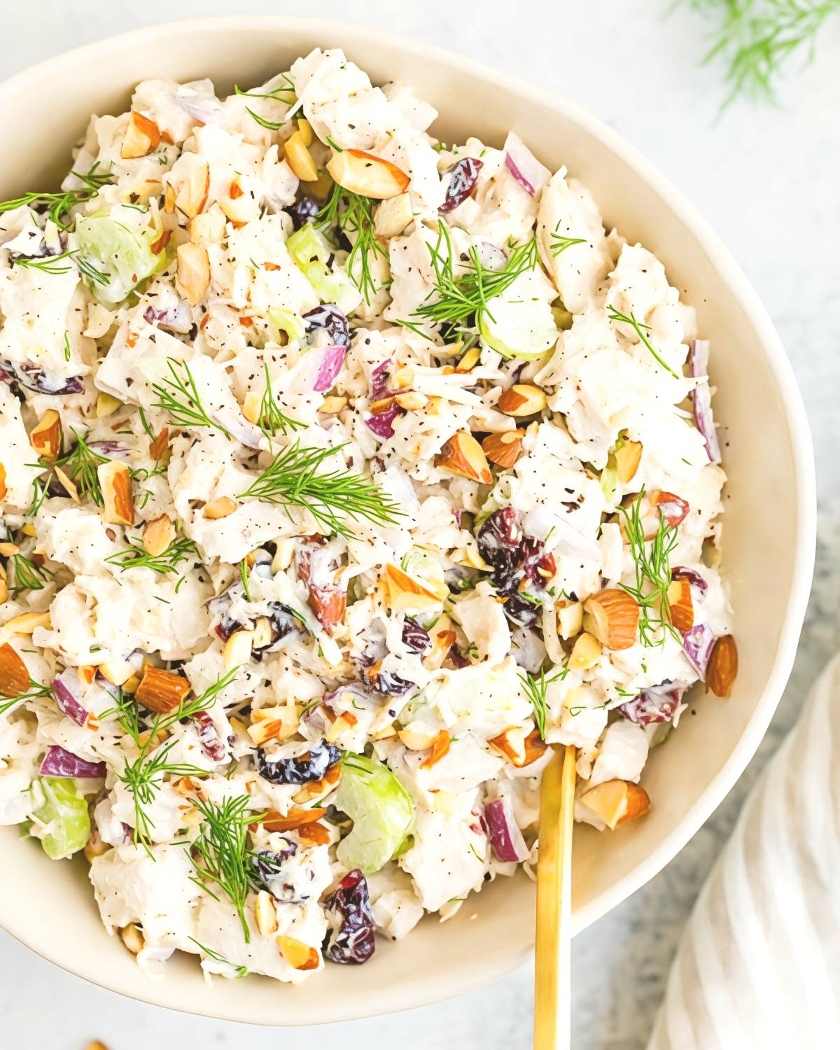 Creamy leftover turkey salad mixed with dried cranberries, chopped almonds, celery, red onions, and fresh dill in a white bowl.