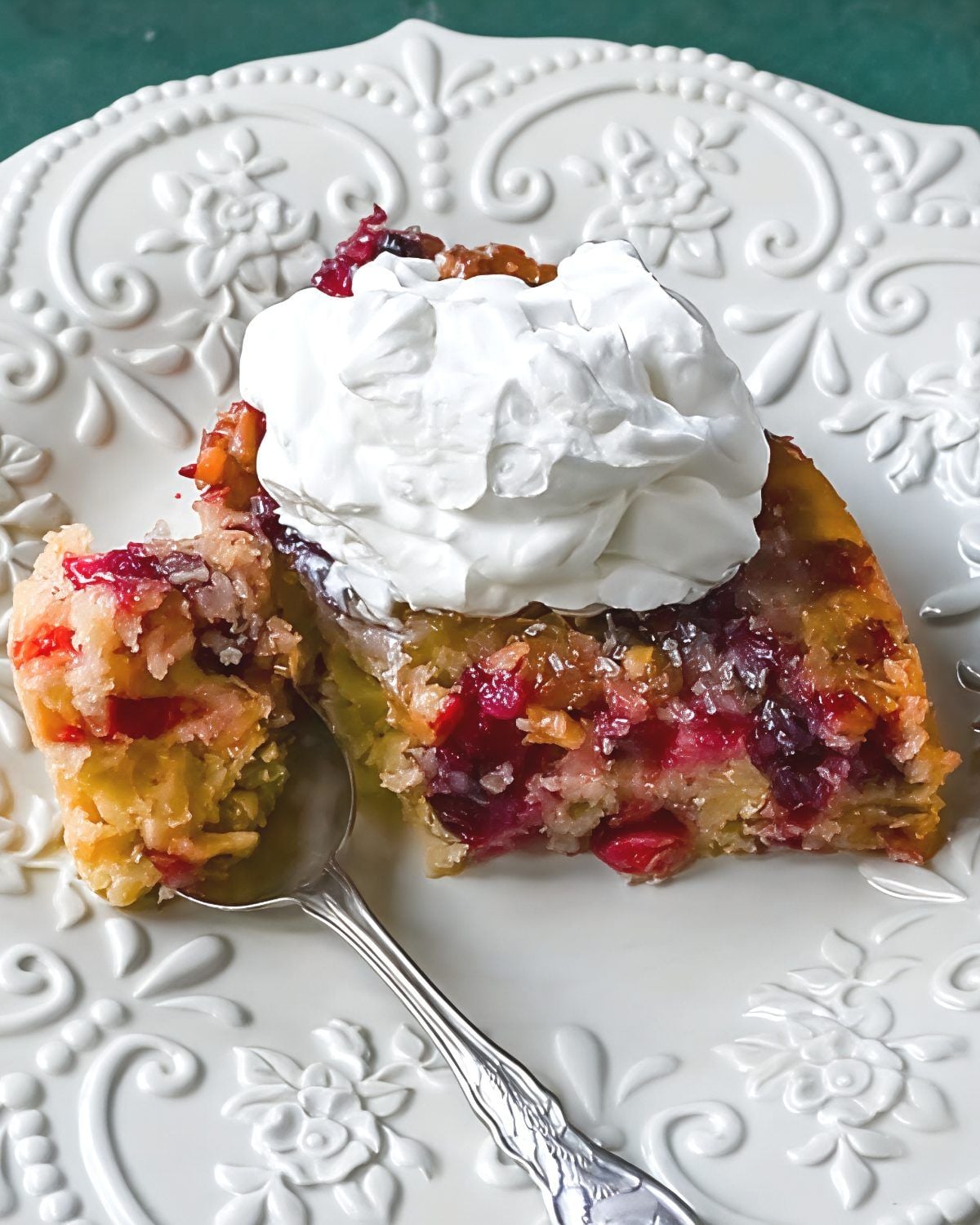 A slice of warm Nantucket cranberry pie packed with tart whole cranberries and chopped walnuts, topped with a generous dollop of whipped cream on an ornate ceramic plate.
