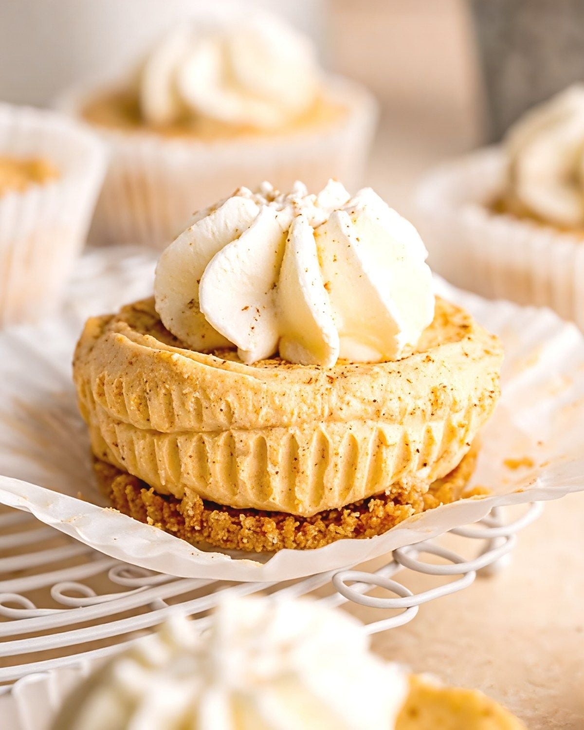 Individual no-bake mini pumpkin cheesecakes set in graham cracker crusts, topped with swirls of whipped cream and a sprinkle of cinnamon, served on a festive platter.