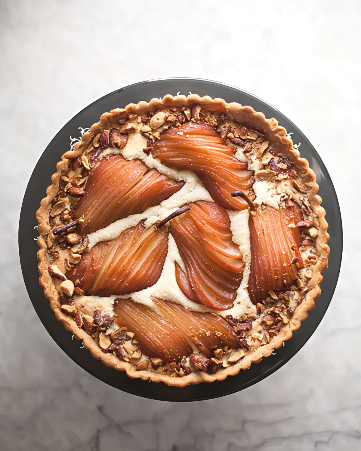 An overhead view of an elegant pear almond tart baked in a fluted pastry shell, arranged with sliced poached pears nestled in frangipane cream and garnished with toasted almonds.