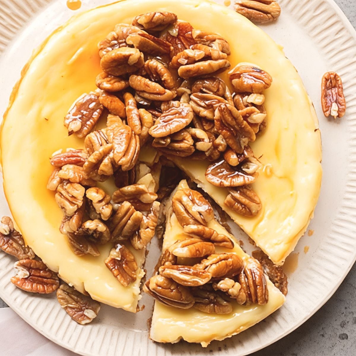 A rich creamy pecan pie cheesecake sliced on a ceramic plate, piled high with glossy caramel-coated toasted pecans.