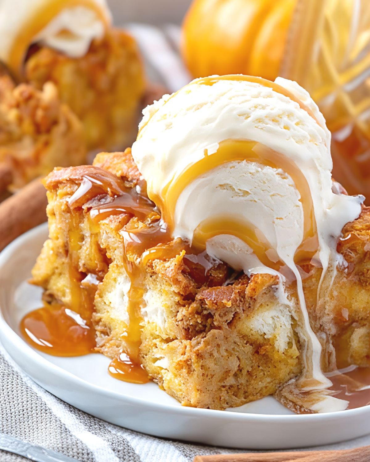 A warm slice of spiced pumpkin bread pudding topped with a scoop of vanilla ice cream and drizzled with rich caramel sauce on a white plate.
